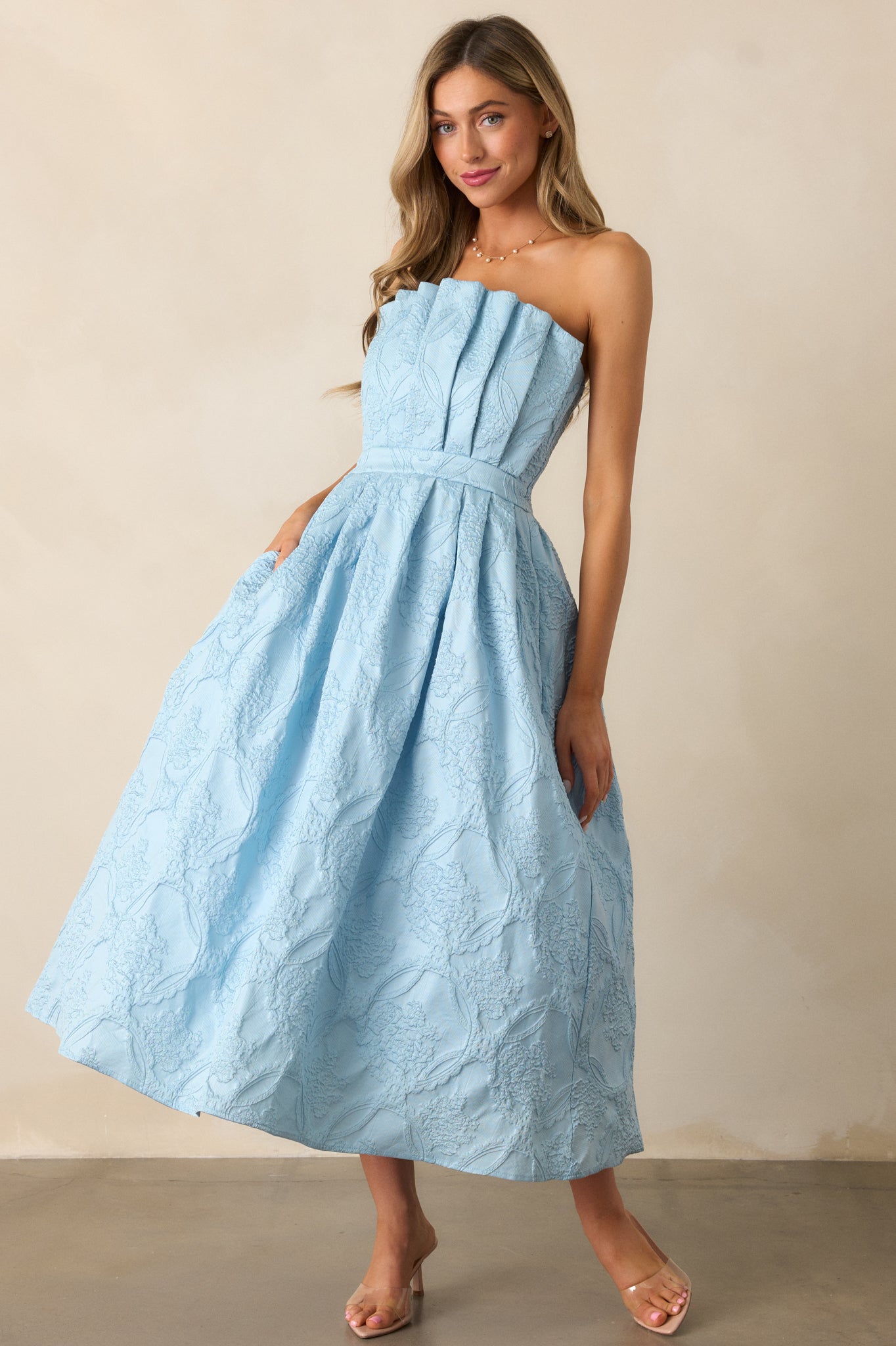 A full view of the sky blue midi dress emphasizing the pleated bodice, pleated skirt, and hip pockets for a chic look.