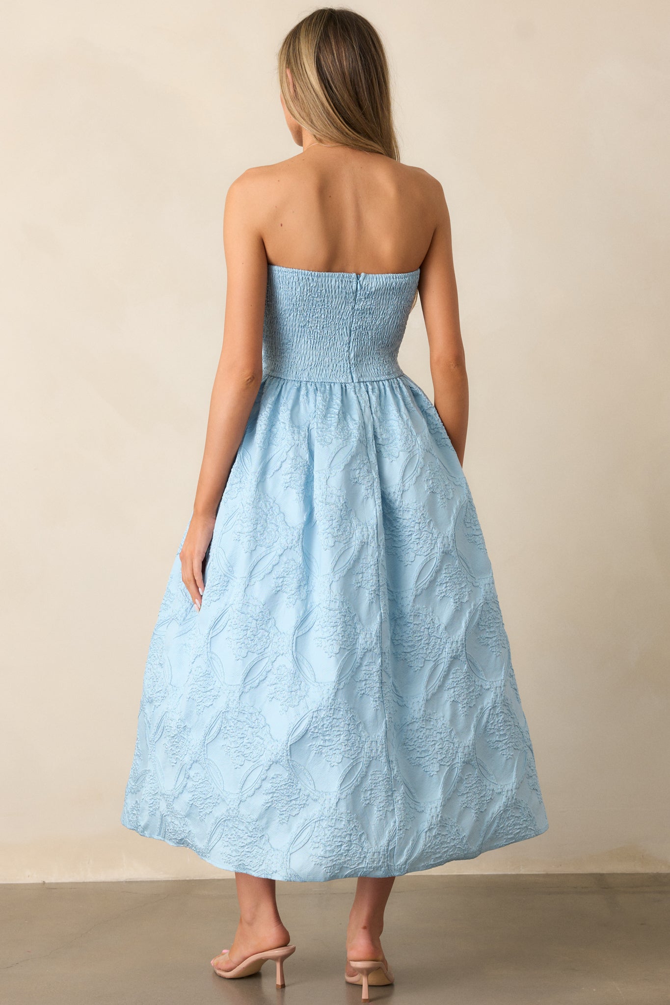 A view of the sky blue midi dress from behind, featuring the smocked back, discrete zipper, and smooth pleats.