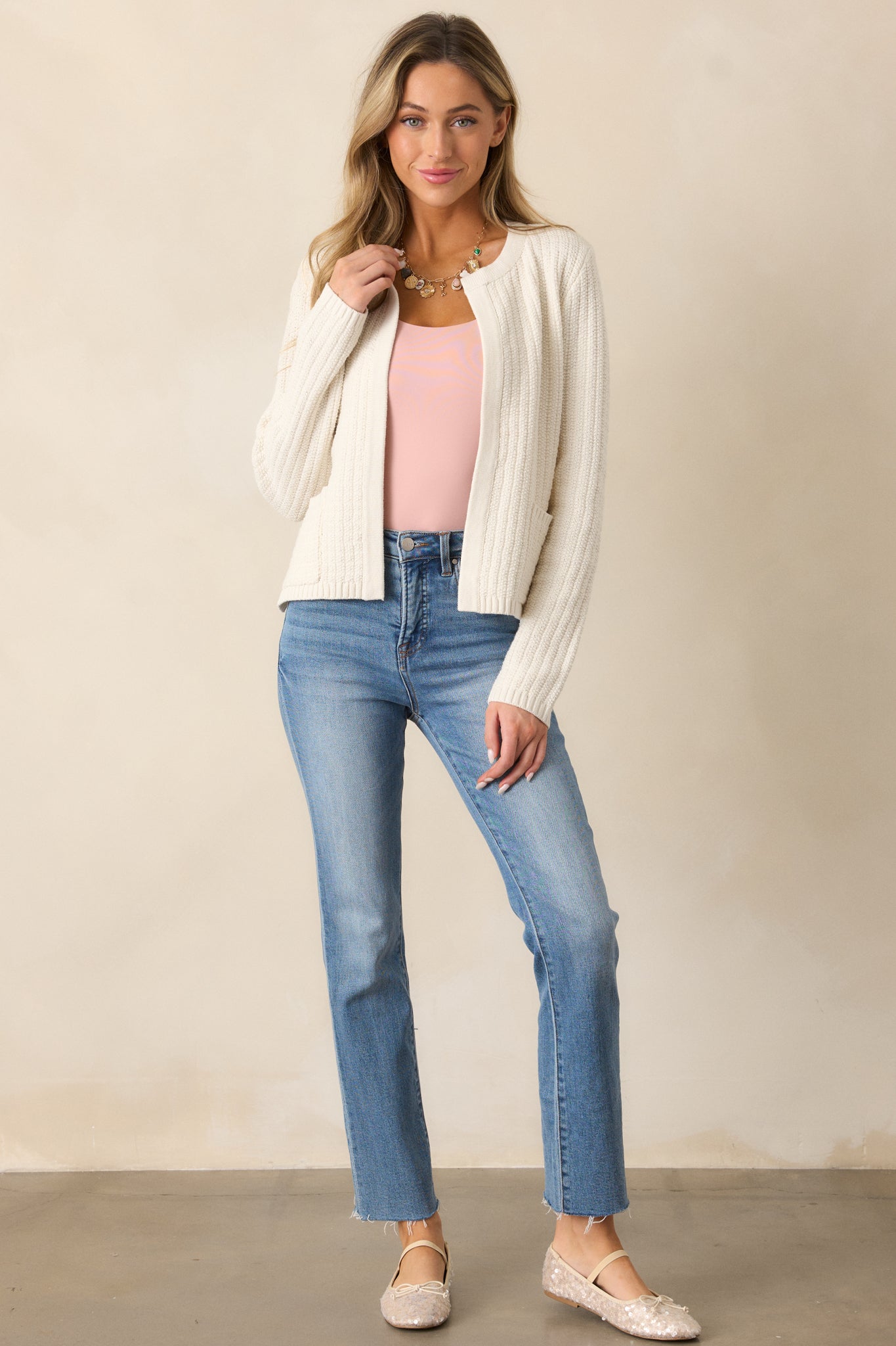 An ivory cardigan with a rounded neckline, long sleeves, and a knit design, featuring functional pockets.