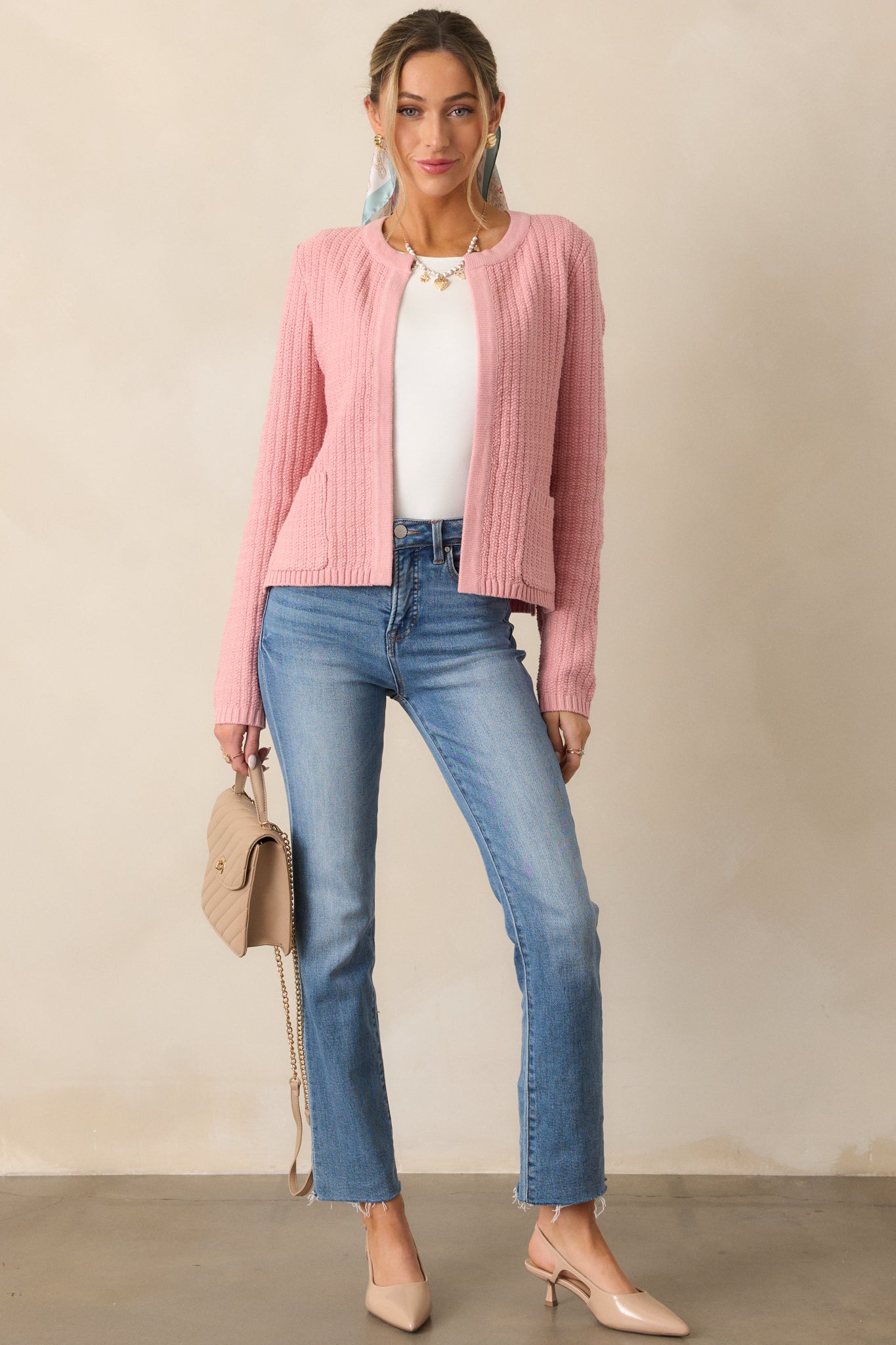 Full view of a rose cardigan with a rounded neckline, long sleeves, and a knit design, shown worn open with visible functional pockets.