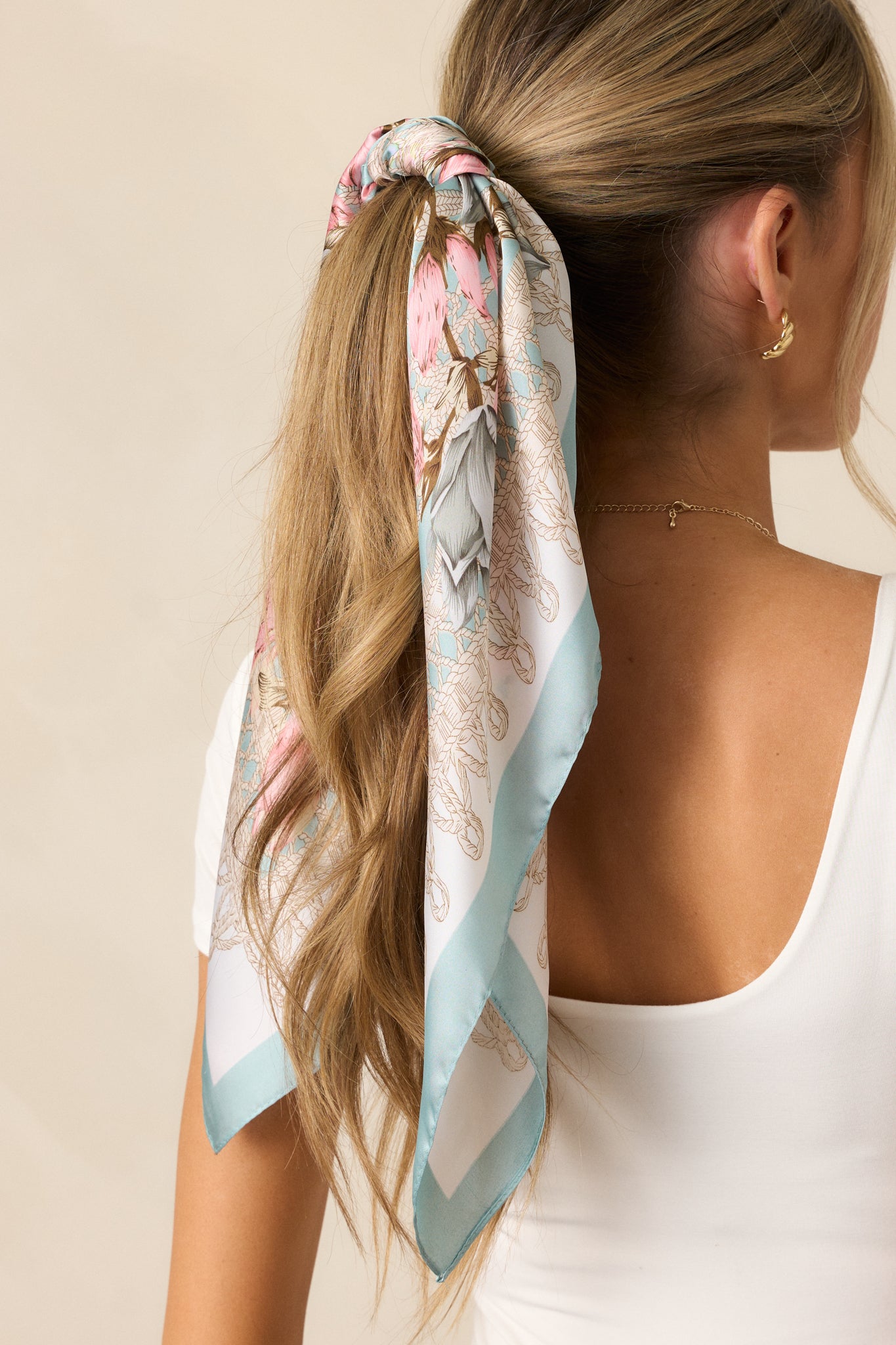 A focused shot of the scarf’s floral pattern, showcasing the blend of pink and blue hues against the rich turquoise background.