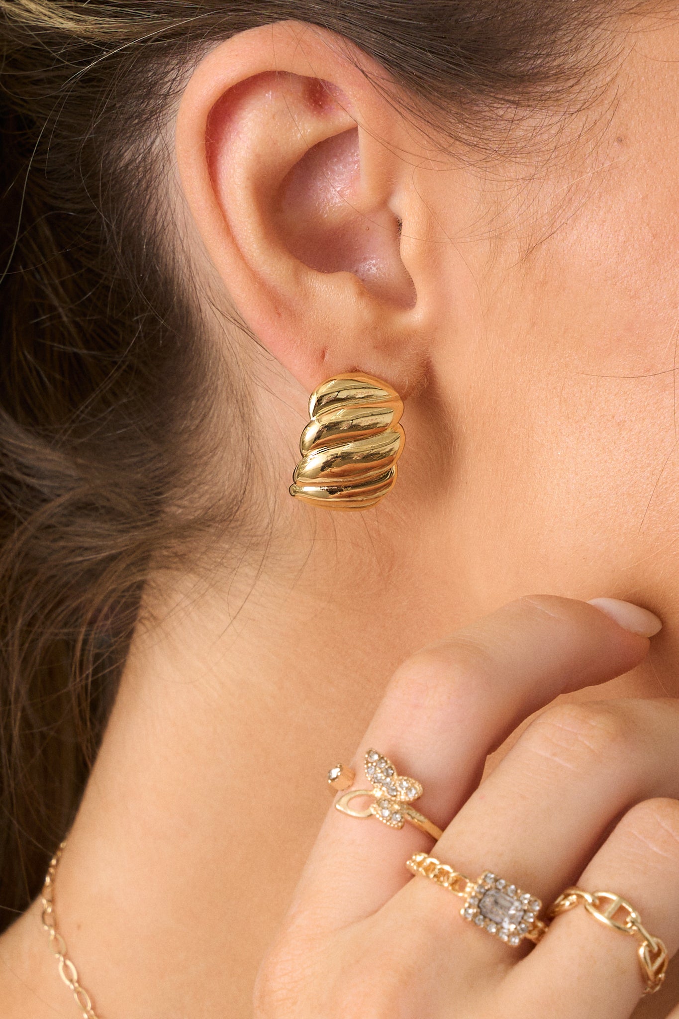 A detailed close-up of the gold earrings, showcasing the textured gold surface, twist design, and the rectangular incomplete hoop shape, with the secure back postings clearly visible.