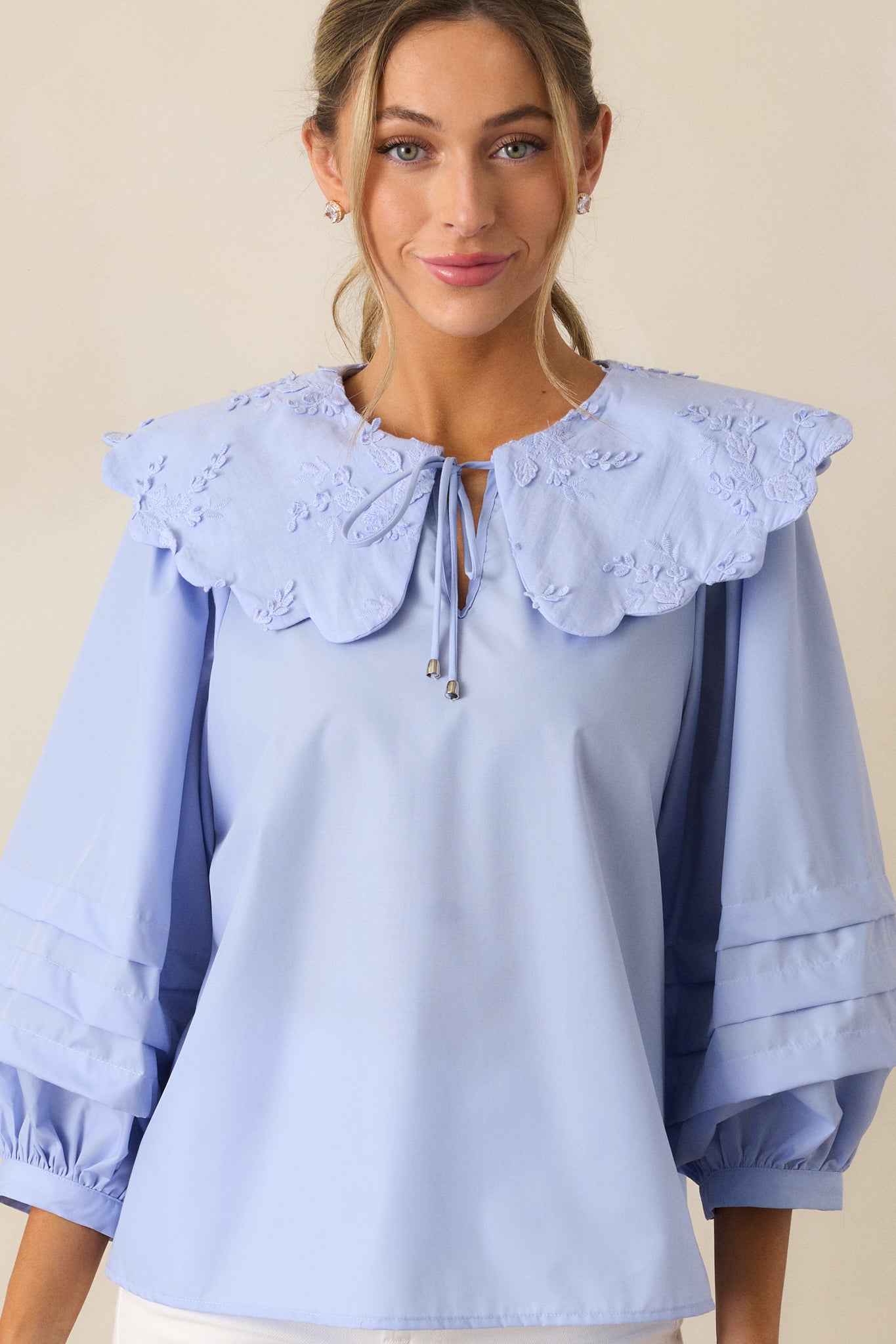 A cropped image of the blouse from the front, focusing on the self-tie keyhole and the floral embroidered scalloped collar.