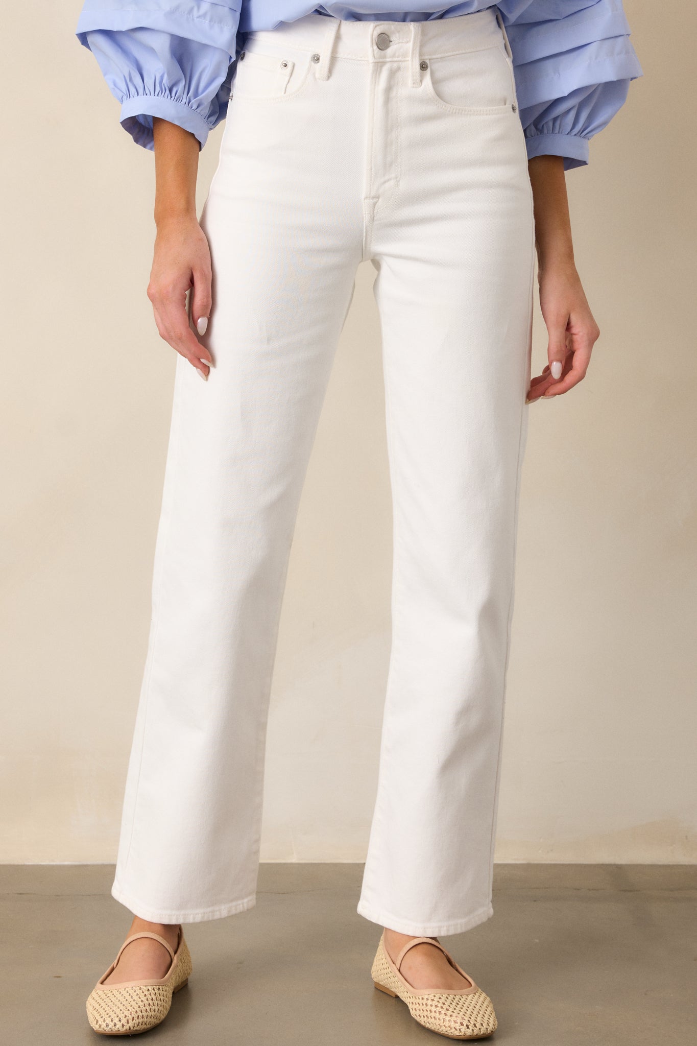 A cropped view of the white jeans, focusing on the waist area, showing the button and zipper closure, and the functional belt loops, with a glimpse of the high-waisted design.