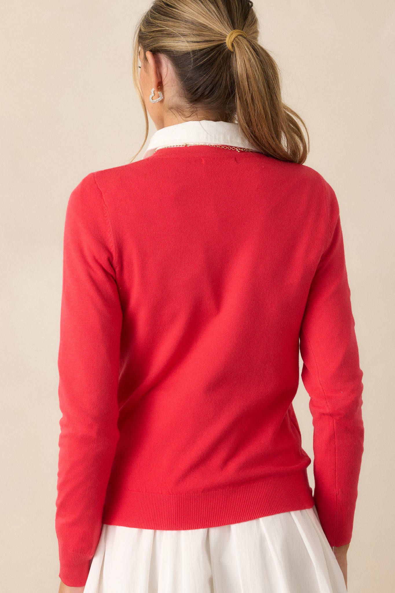 The back view of the red sweater, showing the relaxed fit, long sleeves, and ribbed hem at the bottom of the garment.