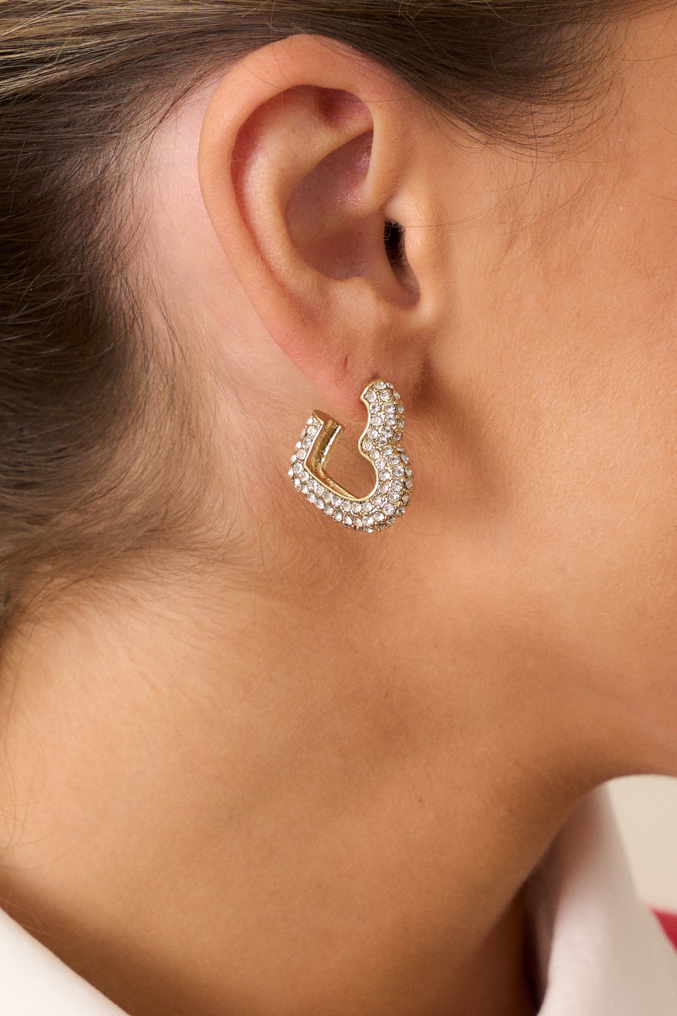 A detailed close-up of the gold heart earring, emphasizing the rhinestone embellishments and the secure back posting.