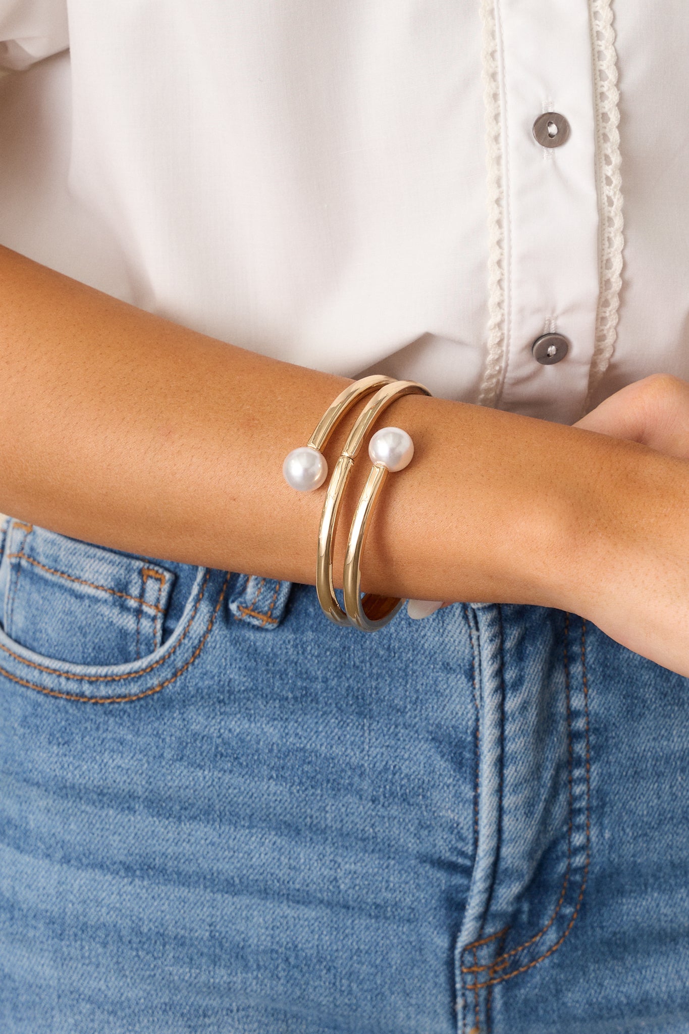 A close-up image of the gold bracelet, emphasizing the two large ivory faux pearls on either end, the snap closure, and the textured layered bangle design, showcasing the bracelet’s elegant and adjustable features.