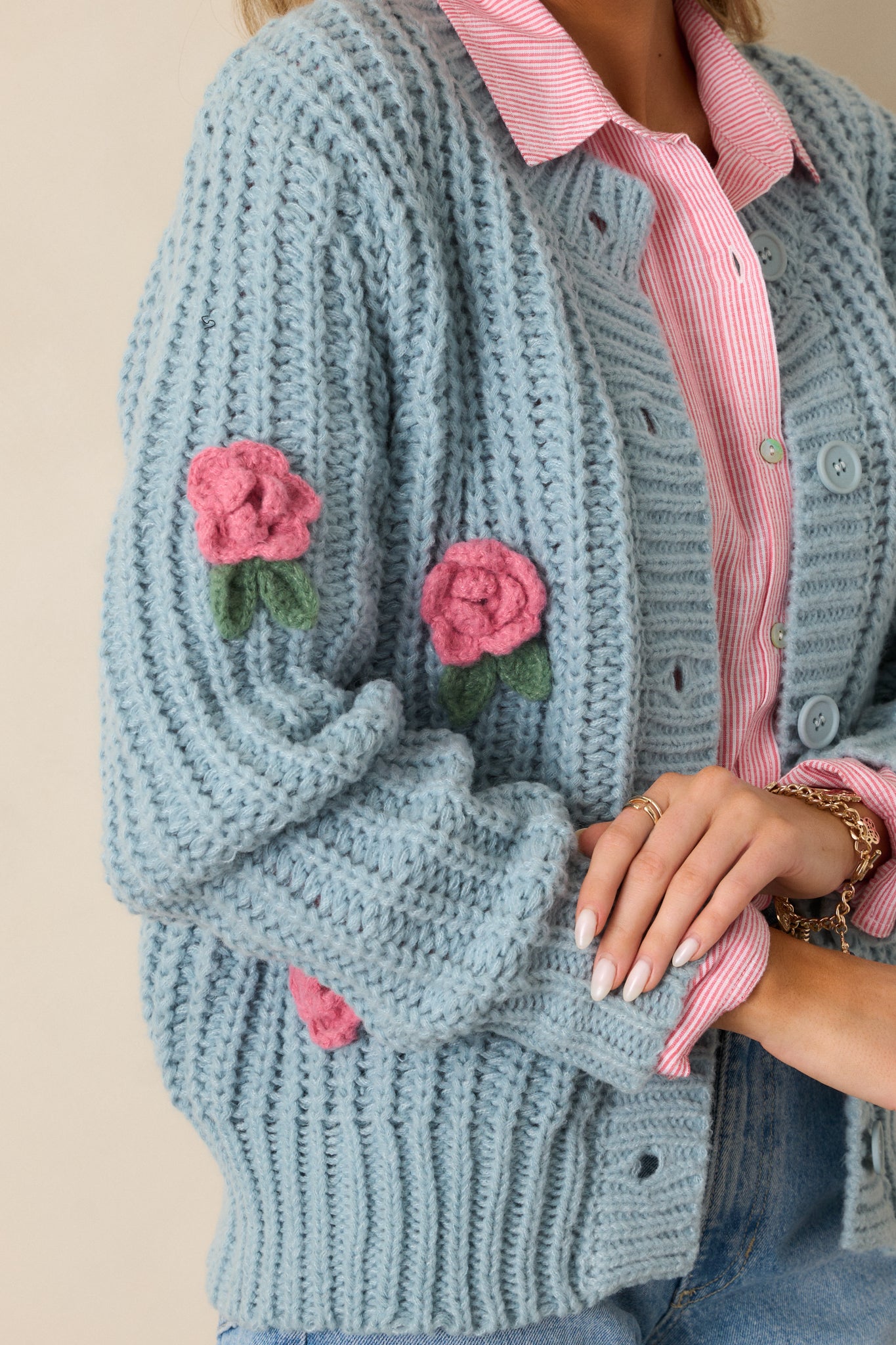 A close-up of the crochet rose detailing along the cardigan's front, showing the fine texture and delicate floral design.