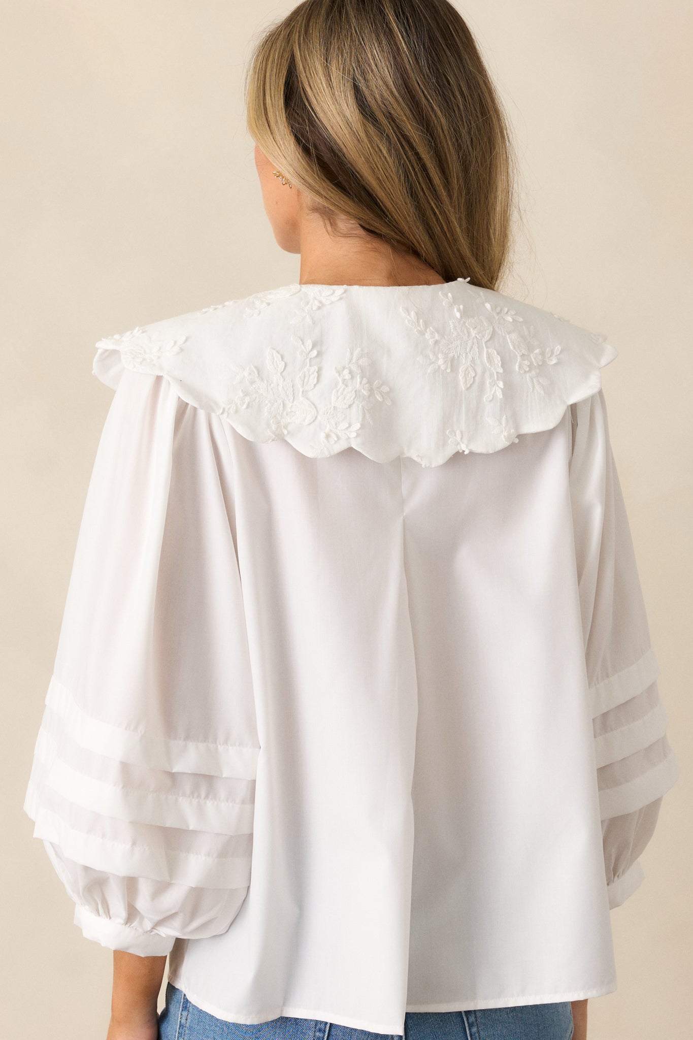 A back view of the ivory blouse, showing the flow of the fabric, the long puff sleeves, scalloped collar, and how the pleated detailing continues down the arm.