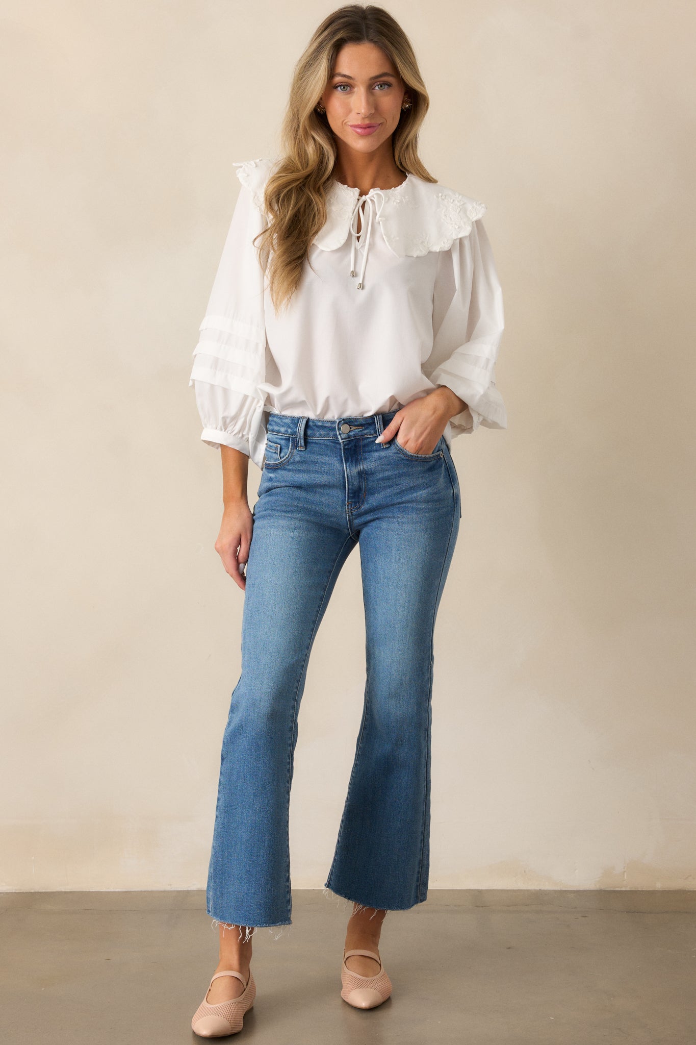 A front-facing view of medium-wash flare jeans, highlighting the cropped raw hem and classic button zipper closure.