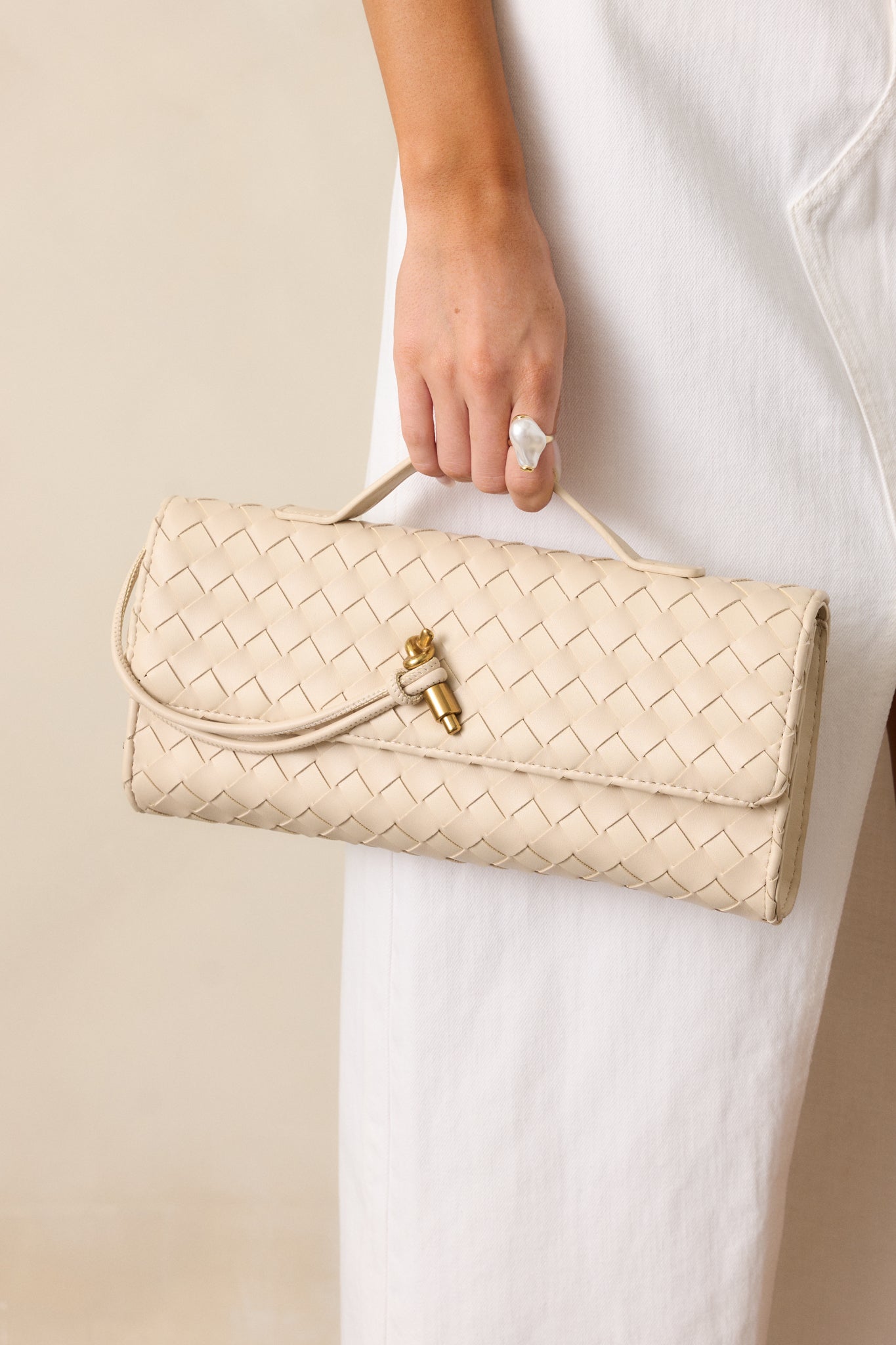 A full shot of the ivory handbag with a rectangular shape, gold hardware, and a top handle, shown with the optional crossbody strap attached.