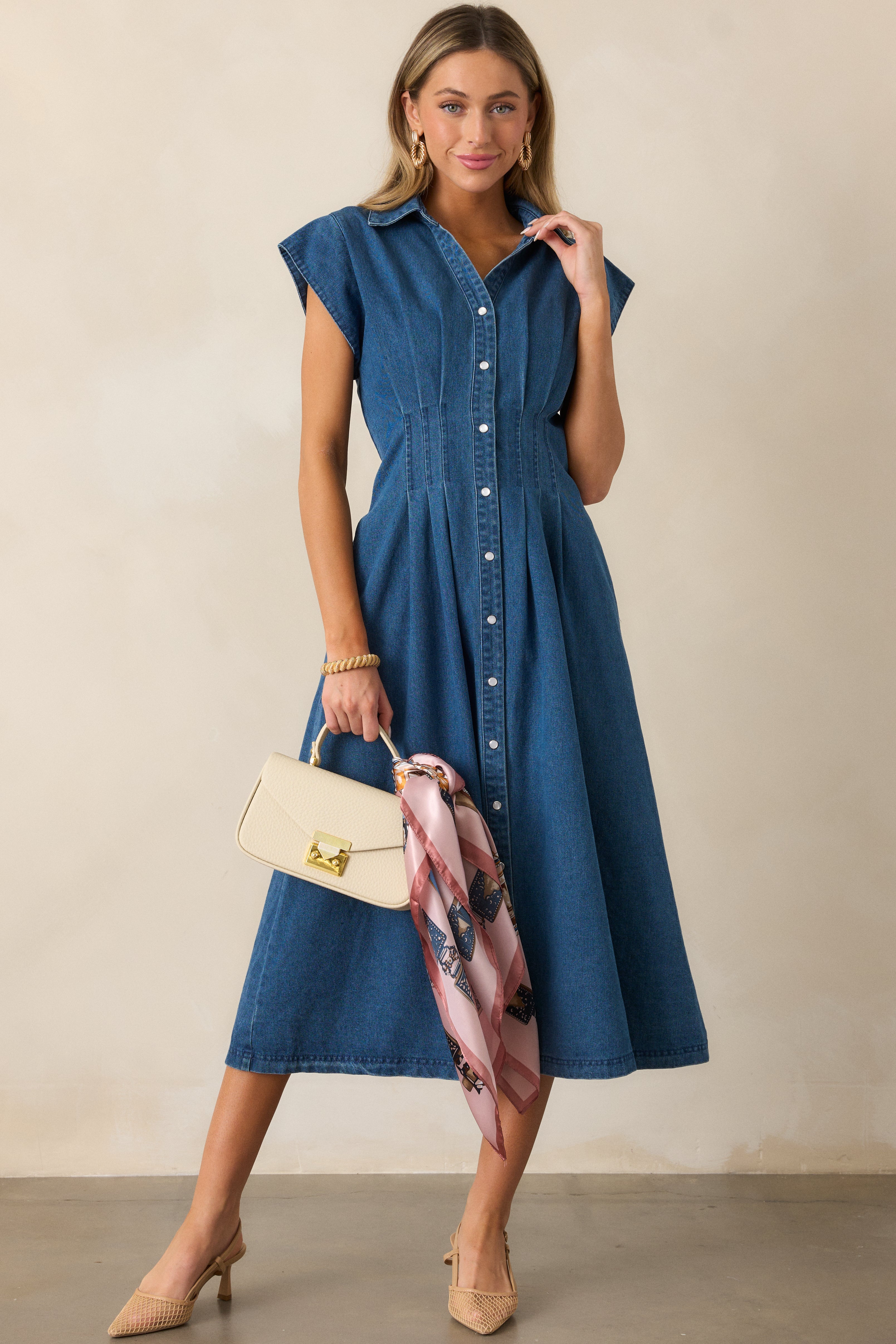 Full view of the dark wash dress highlighting its cap sleeves, pearlized button closures, and pleated waist detail.