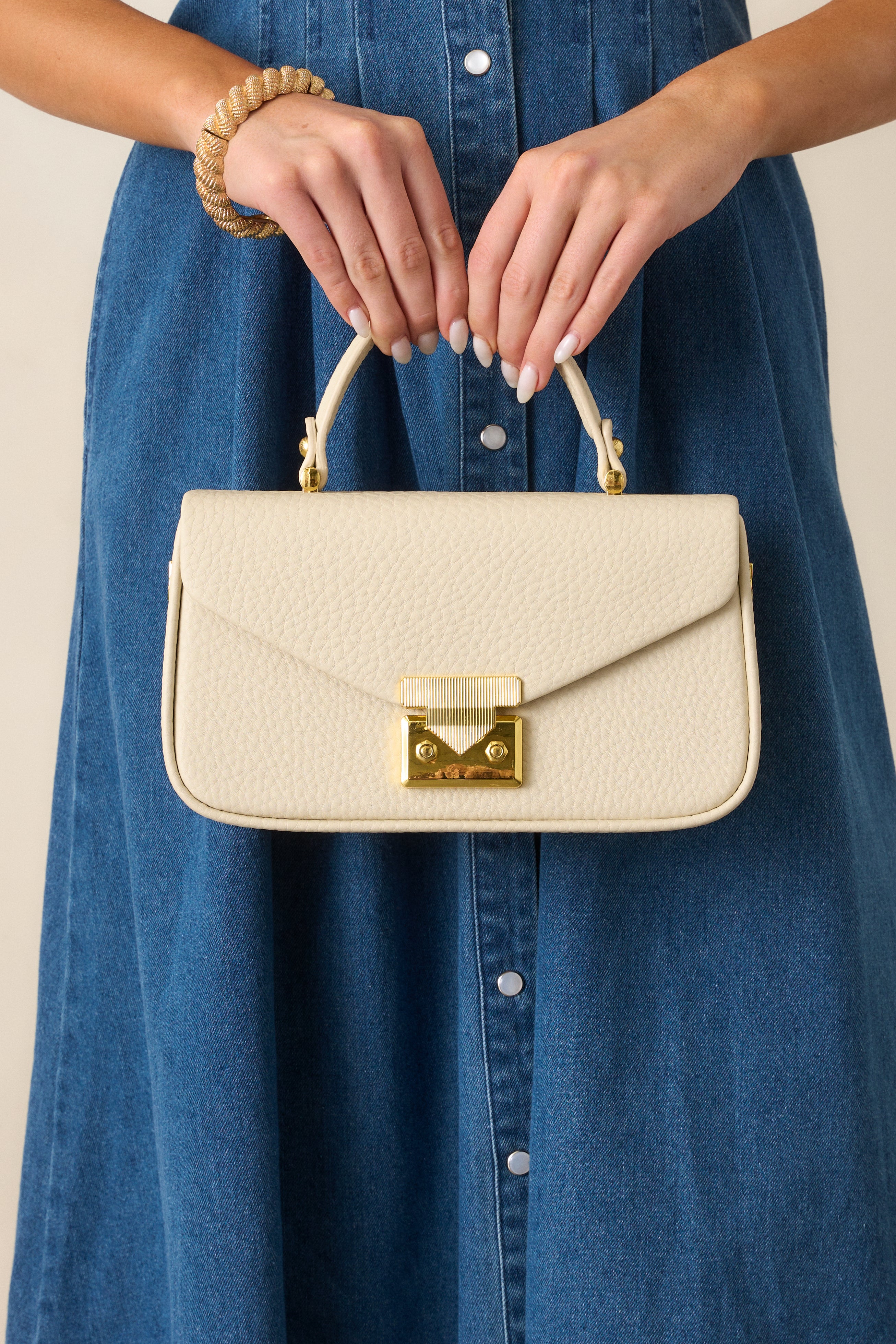 Focused image of the ivory handbag's front, emphasizing the gold hardware and clean rectangular design.