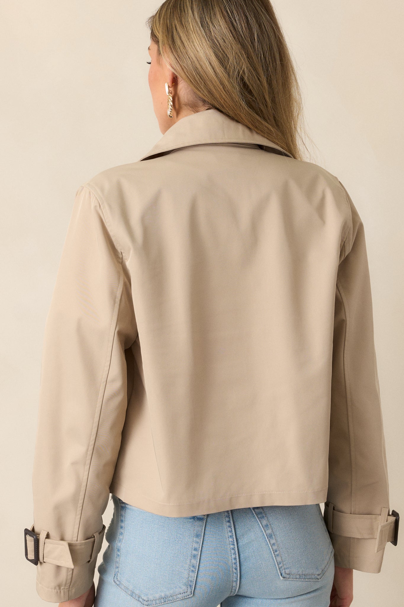 The back view of the khaki coat, emphasizing its cropped silhouette and clean lines, along with the buckle accents on the sleeves.