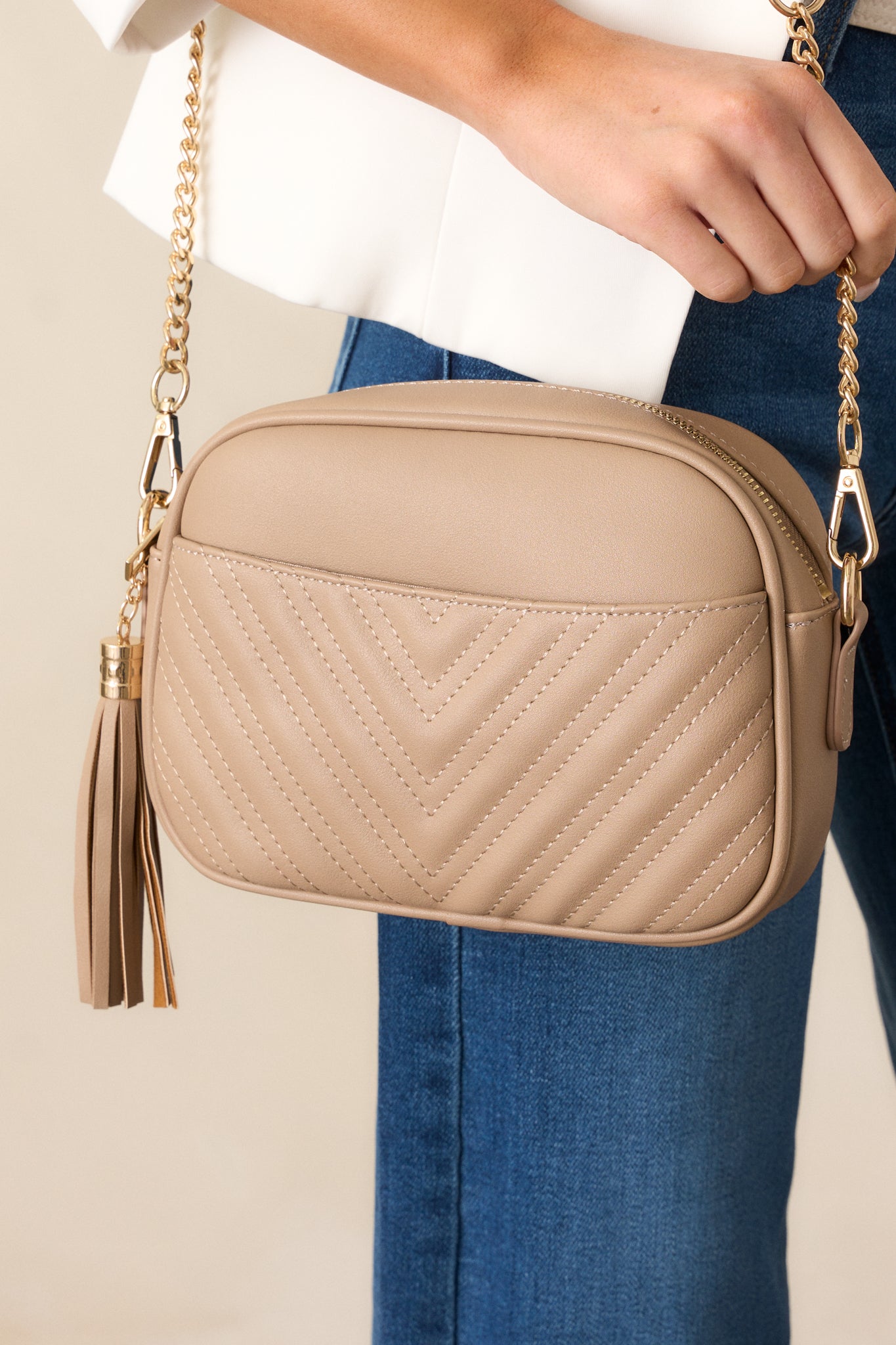 Front view of this bag that features a rounded square design, removable crossbody strap, a removable tassel detail, a zipper closure, an outside slip pocket, and two pockets on the inside.