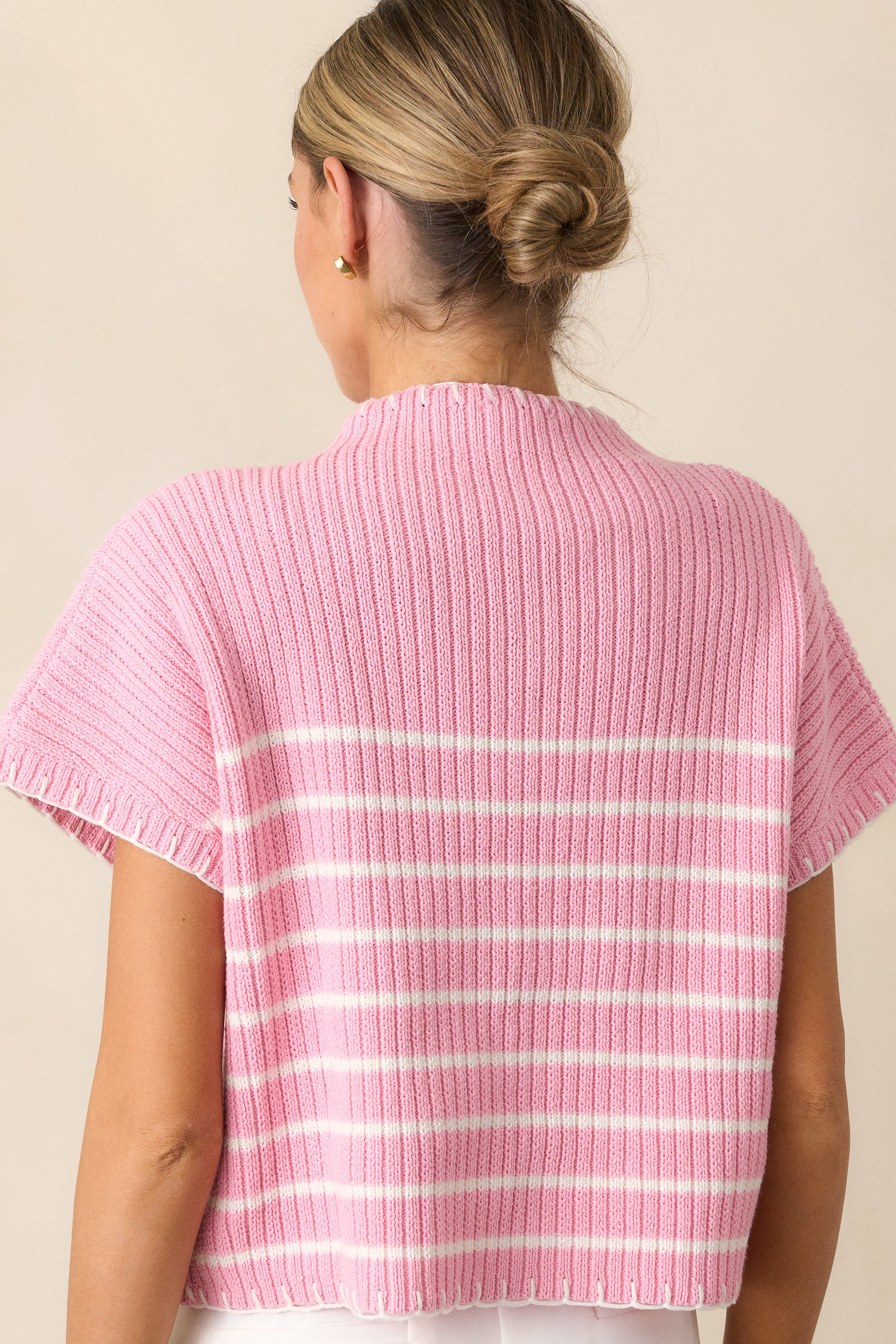 A back view of the pink sweater, highlighting its seamless construction and clean design with white whipstitch accents.