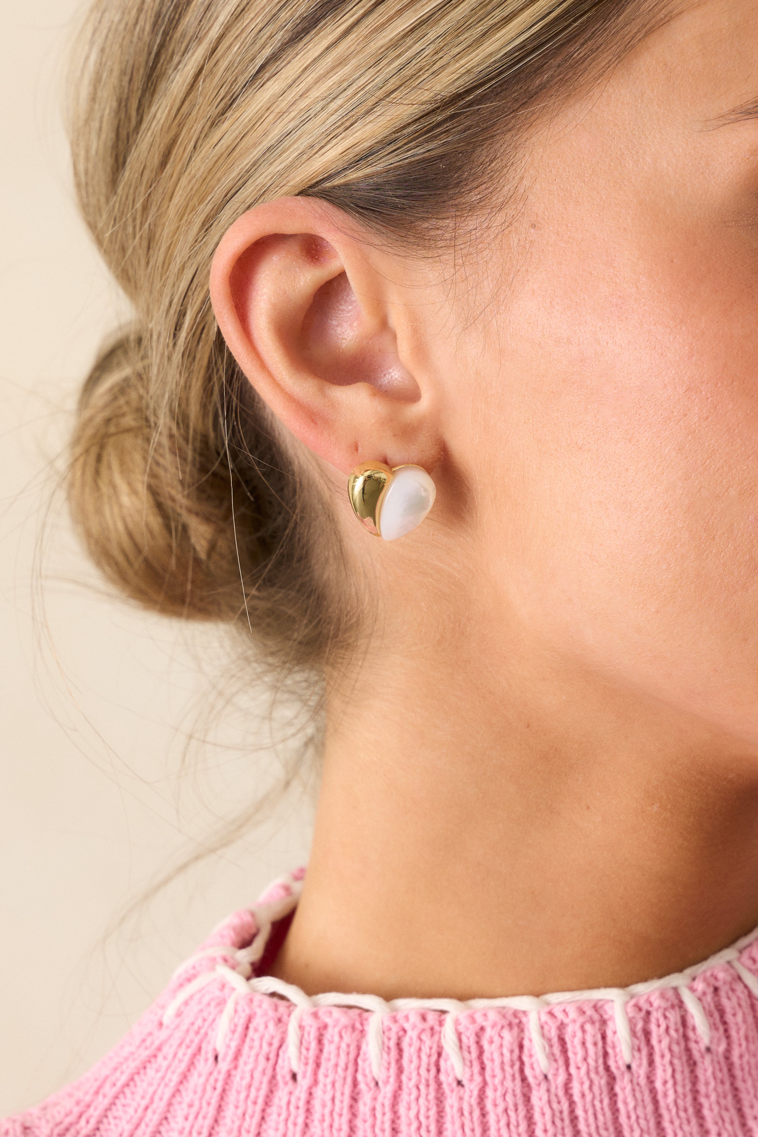 A cropped view of the gold and pearlescent heart stud earrings, showcasing the split gold and ivory faux pearlescent heart design.