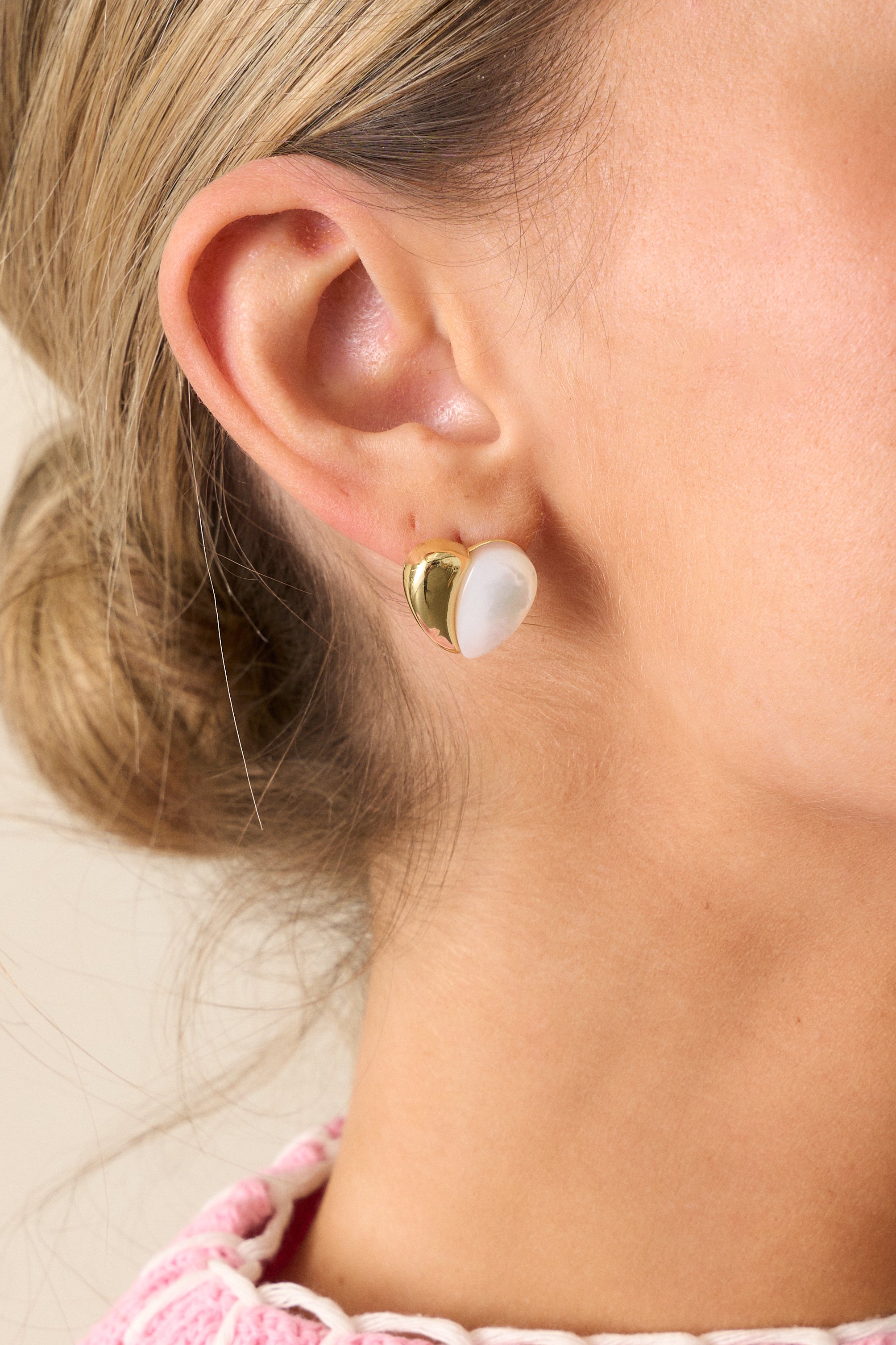 A close-up view of the gold and pearlescent heart stud earrings, emphasizing the gold hardware and the soft pearlescent finish of the heart design.