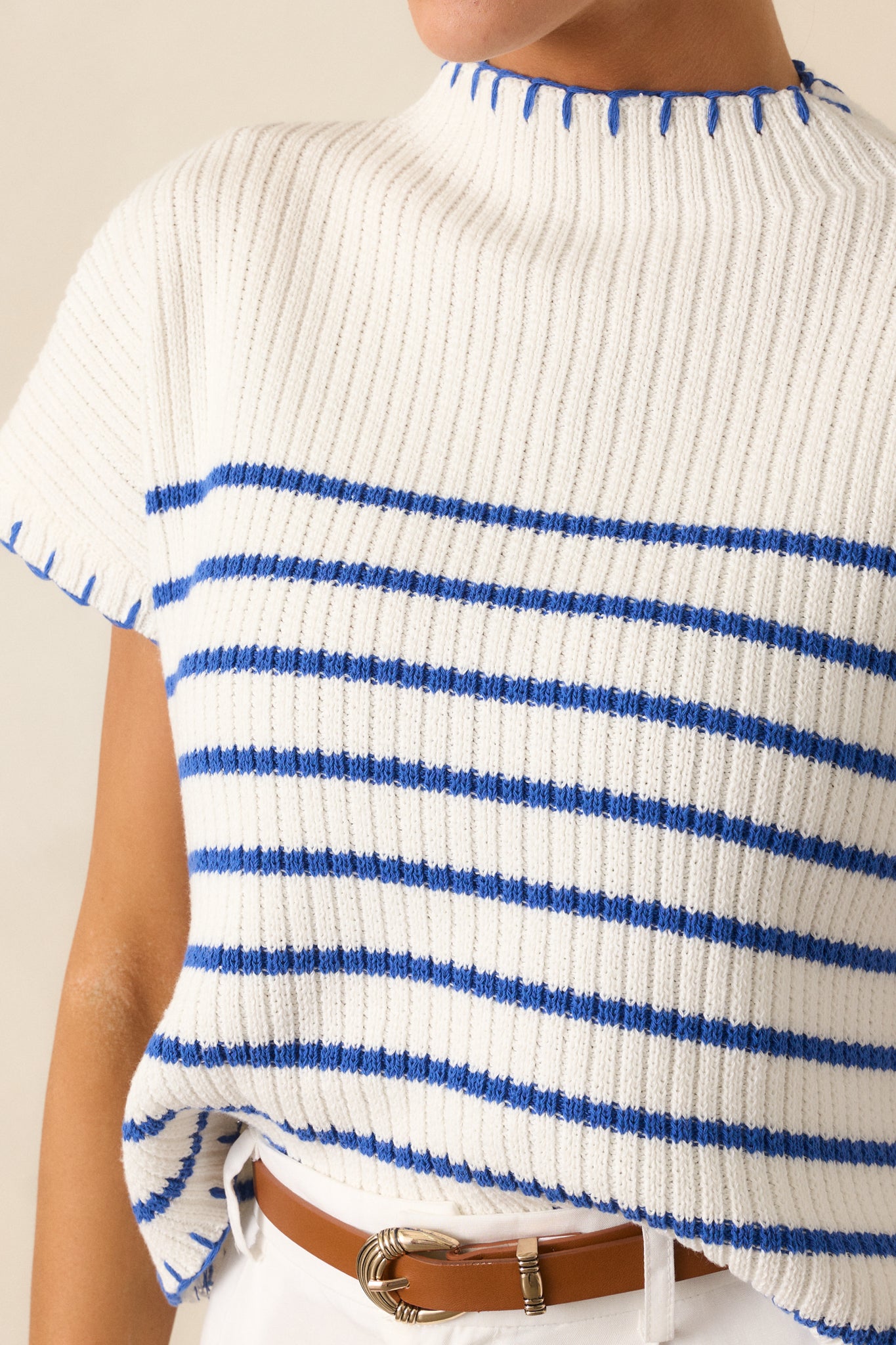 A close-up view of the white sweater's blue whipstitch detailing on the hem, showcasing its intricate craftsmanship.