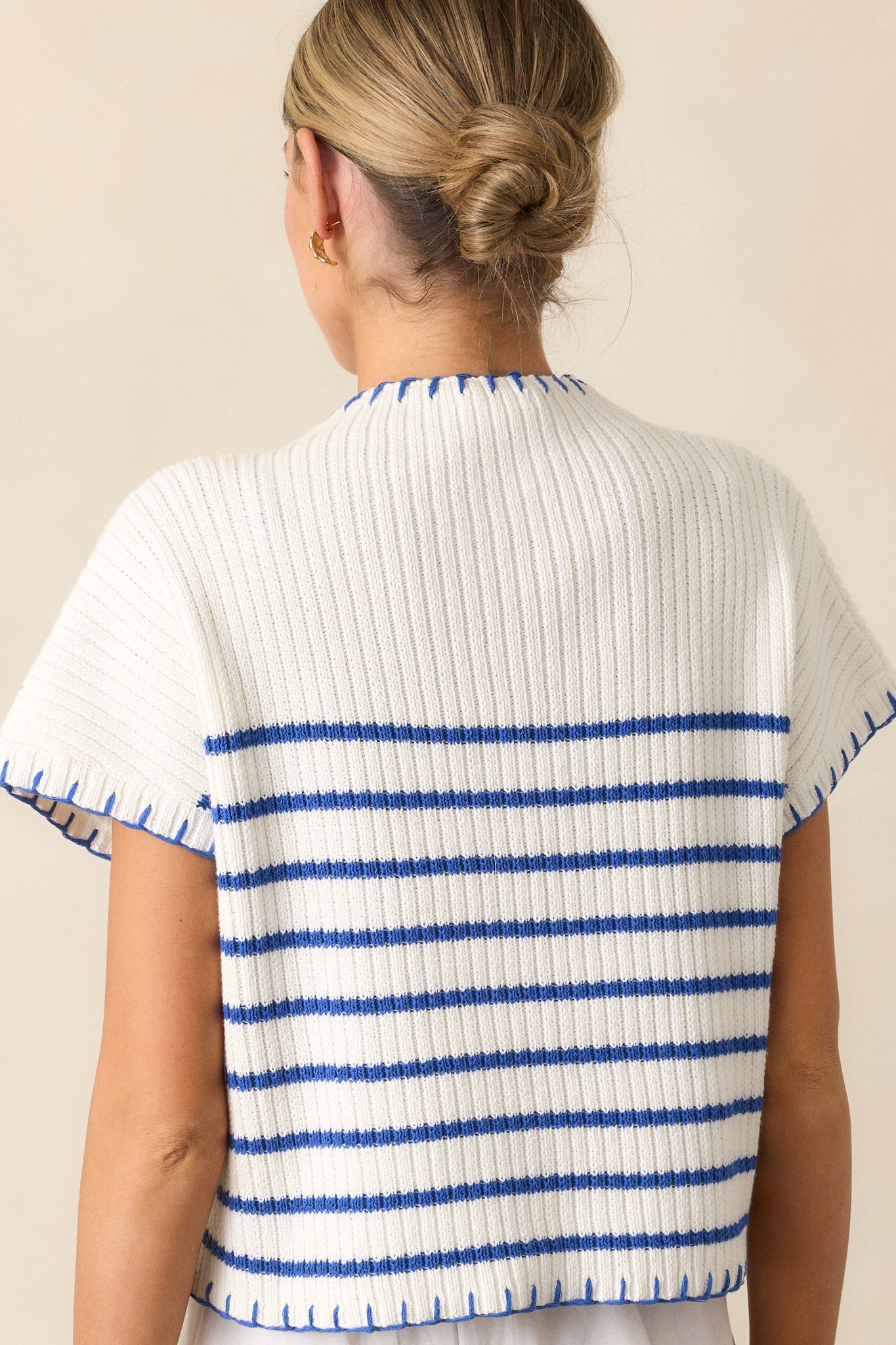 A back view of the white sweater, highlighting its seamless construction and clean design with blue whipstitch accents.