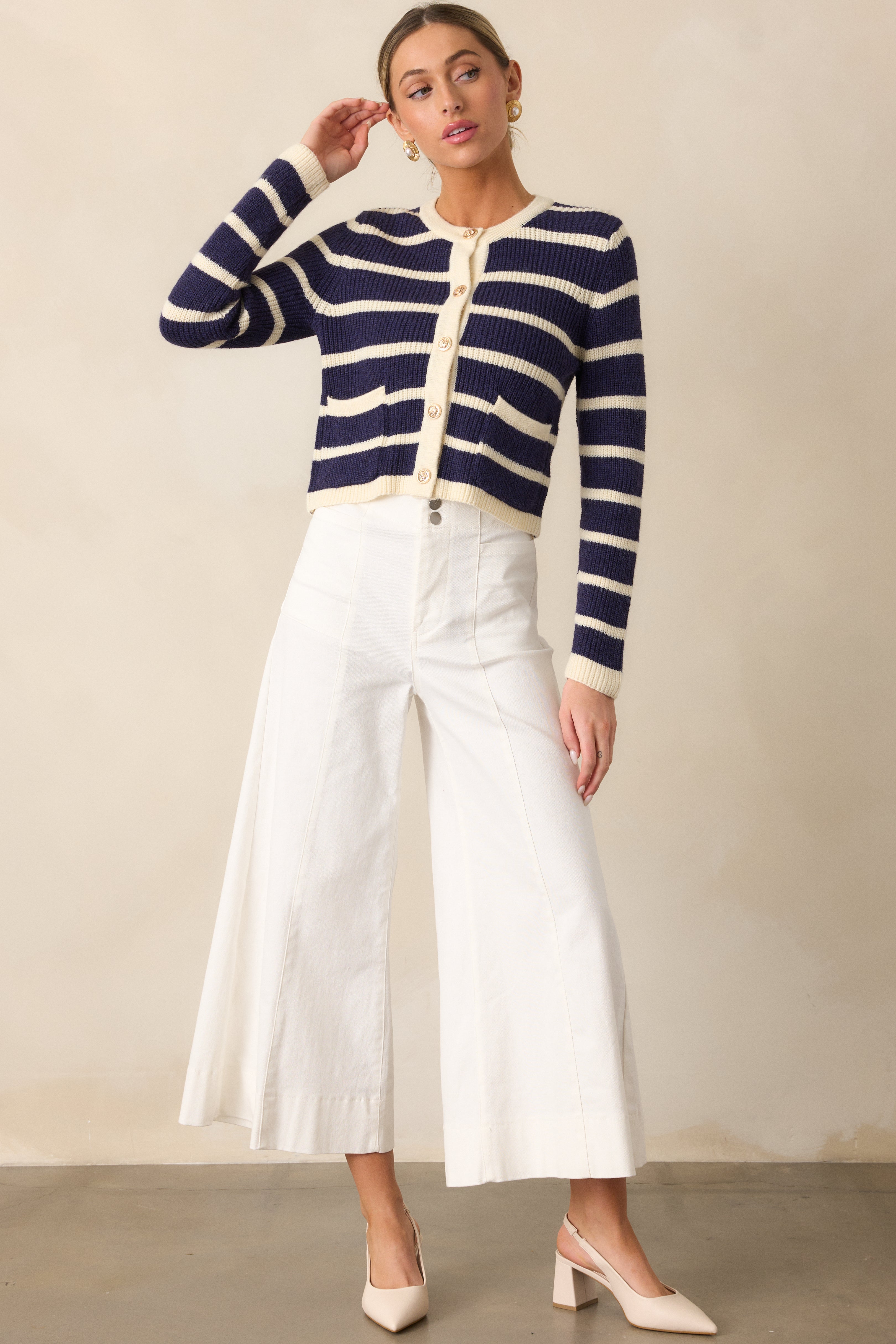 A full-length view of a navy stripe cardigan featuring functional metallic buttons, two patch pockets, and a cropped length.