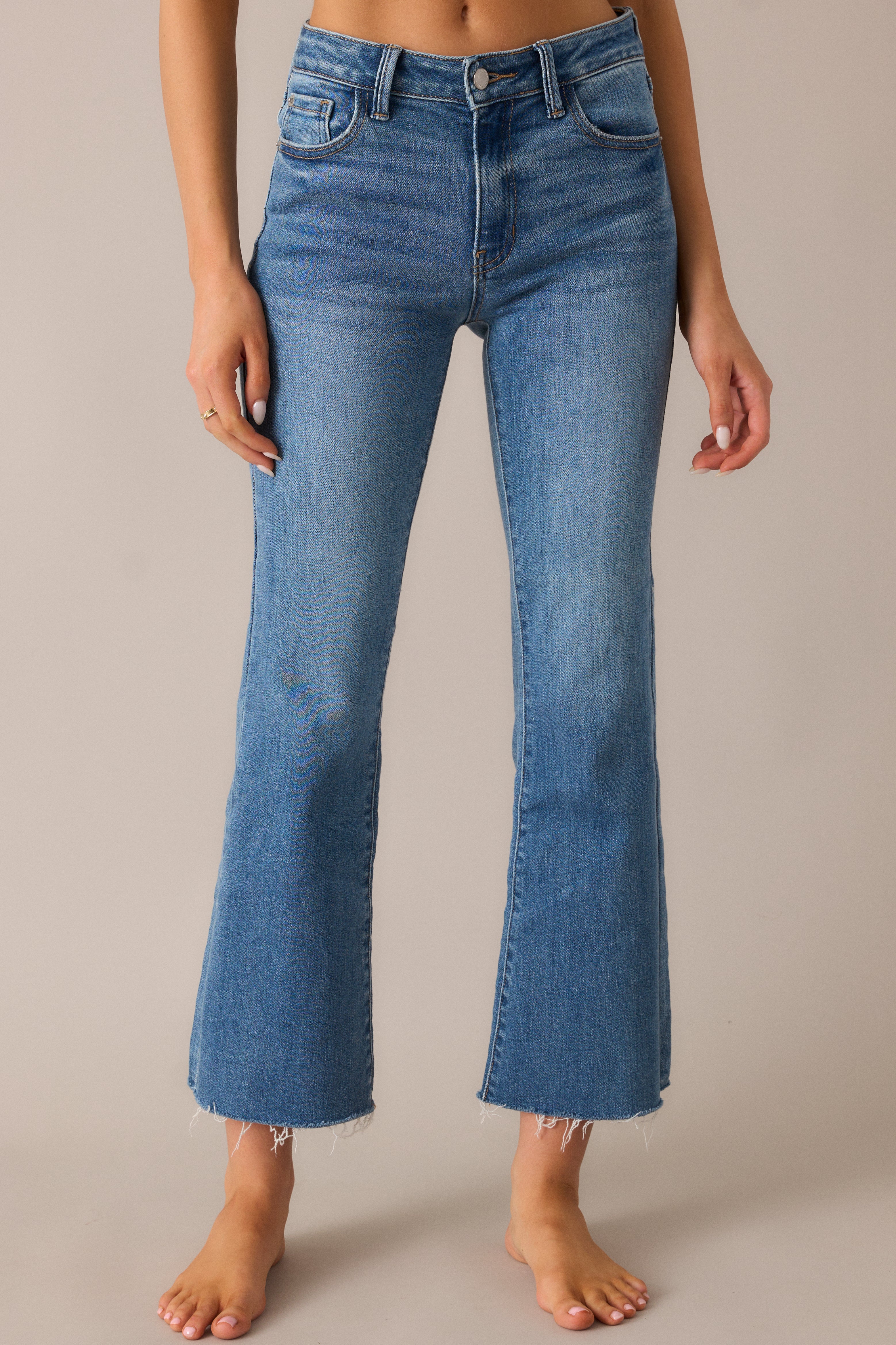 Close-up of the flare leg design and cropped raw hem, showcasing the fashionable, edgy cut of the medium-wash jeans with a classic button-zipper closure.