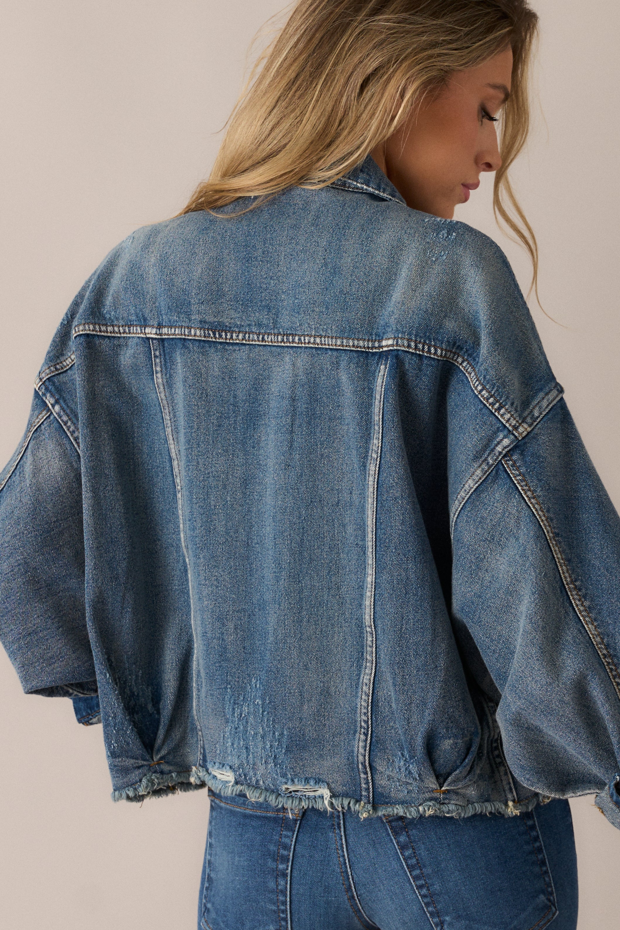 The denim jacket from the back, emphasizing the sweeping dolman sleeves and artfully distressed fabric.