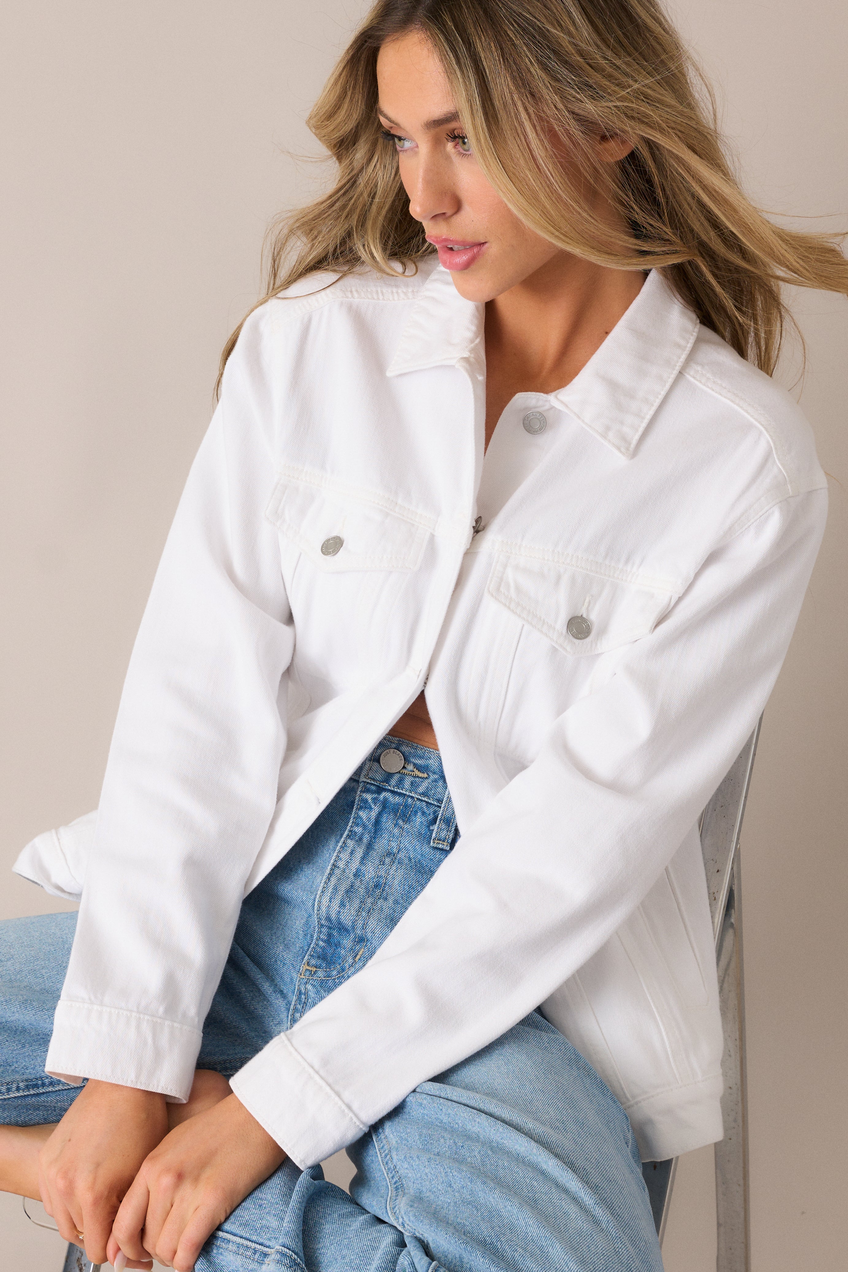  Detailed view of the white denim jacket’s button accents and chest pockets, adding structure and a practical touch to the soft fabric.