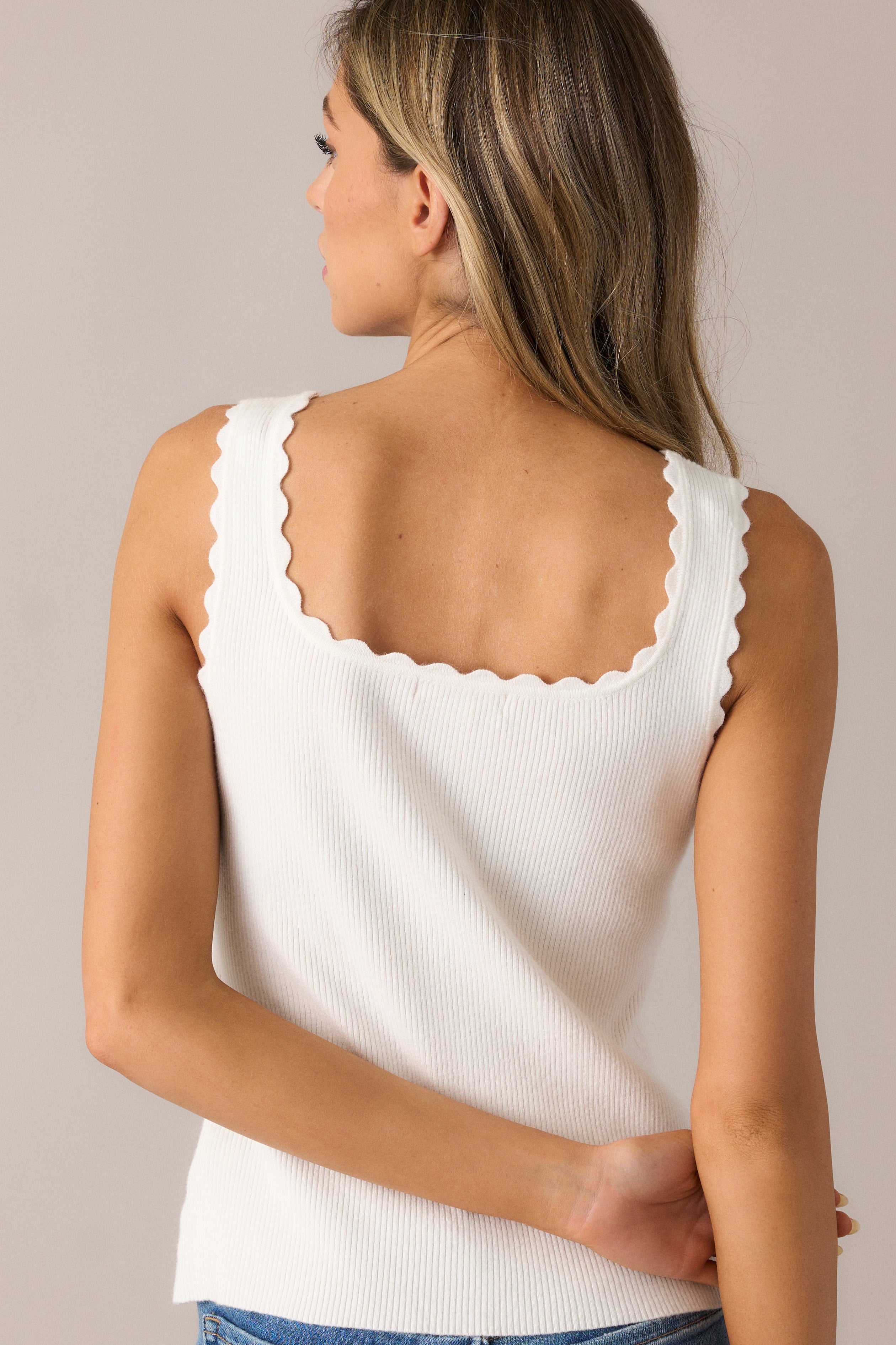 The ivory tank top from the back, showcasing its clean, sleek design with the ribbed fabric and sleeveless cut, complemented by the delicate scalloped hem.