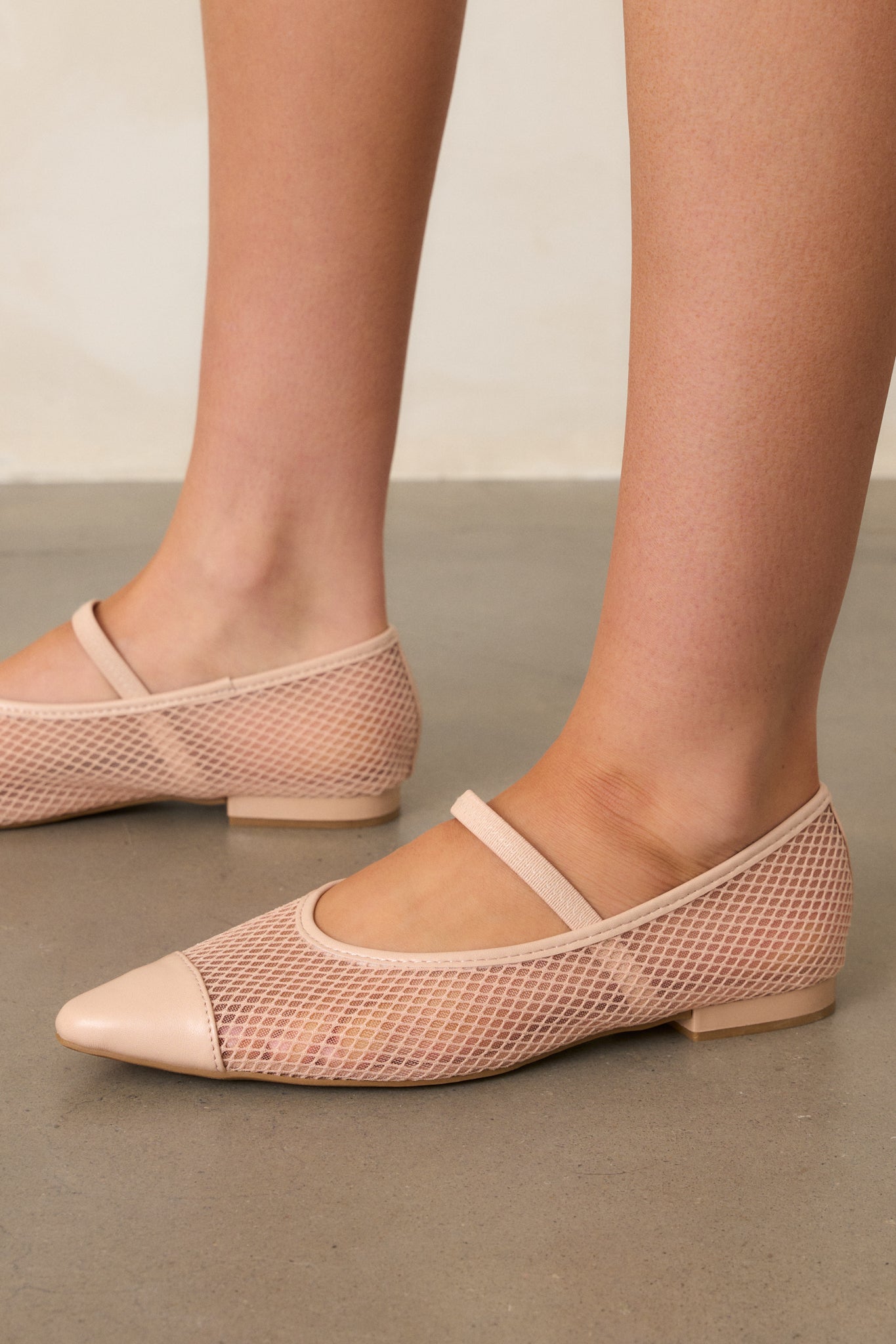 A detailed close-up of the beige mesh flats, showcasing the pointed toe, the fishnet mesh sides, and the elastic foot strap, with the beige trim and small heel clearly visible along with the cushioning in the sole.