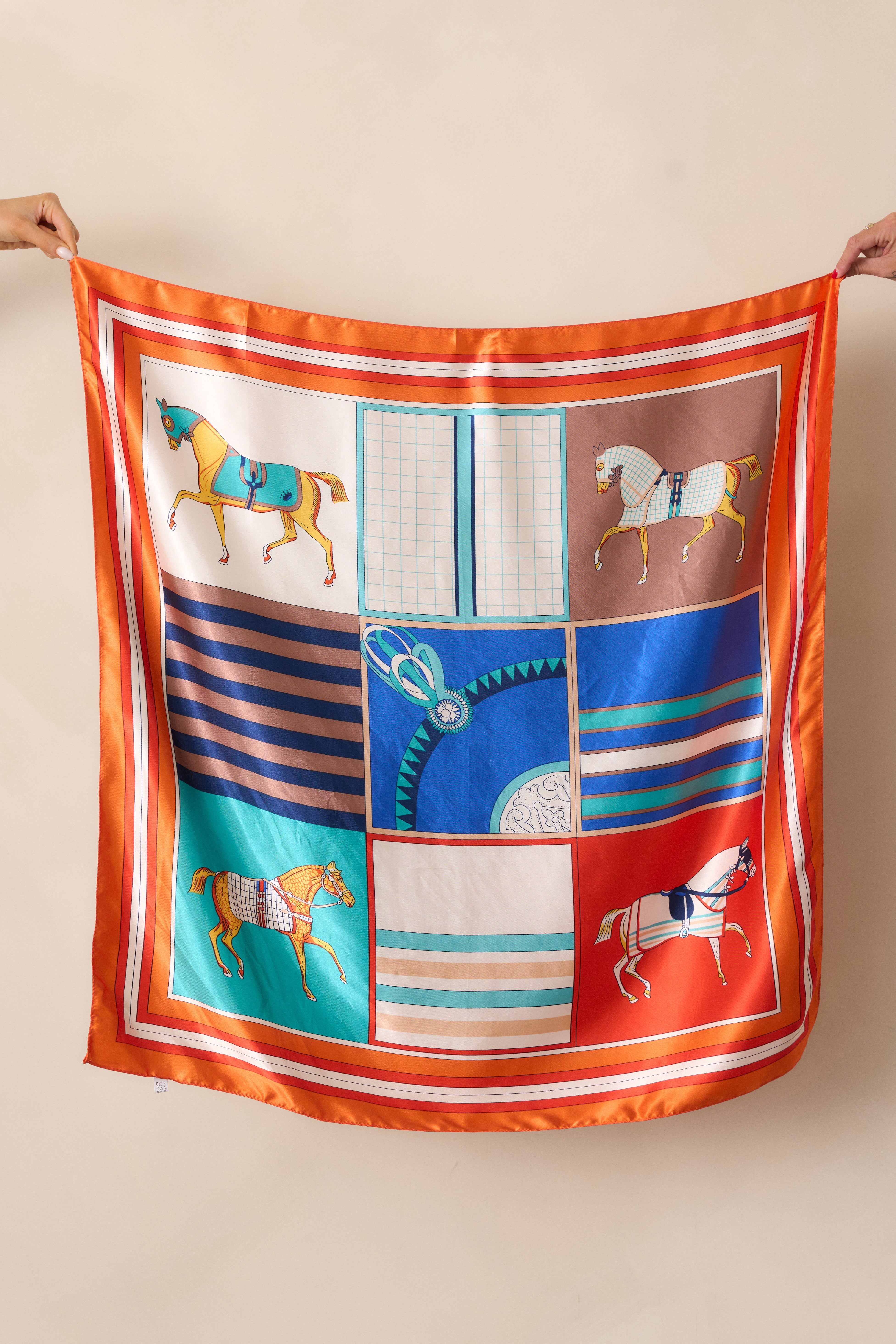 Cropped view of the orange scarf focusing on the detailed horse design and contrasting trim in ivory, teal, and yellow.