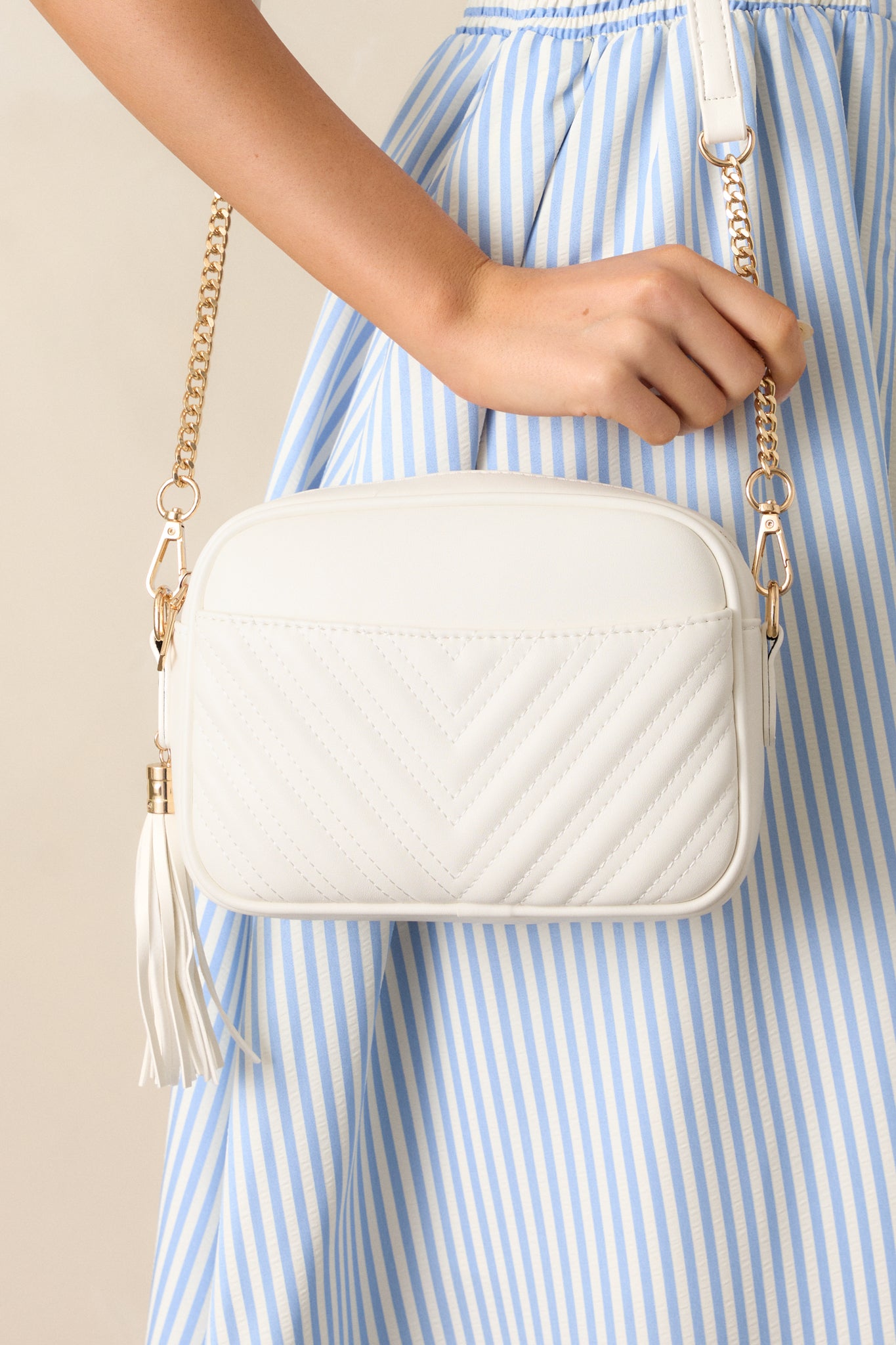 Front view of this bag that features a rounded square design, removable crossbody strap, a removable tassel detail, a zipper closure, an outside slip pocket, and two pockets on the inside.