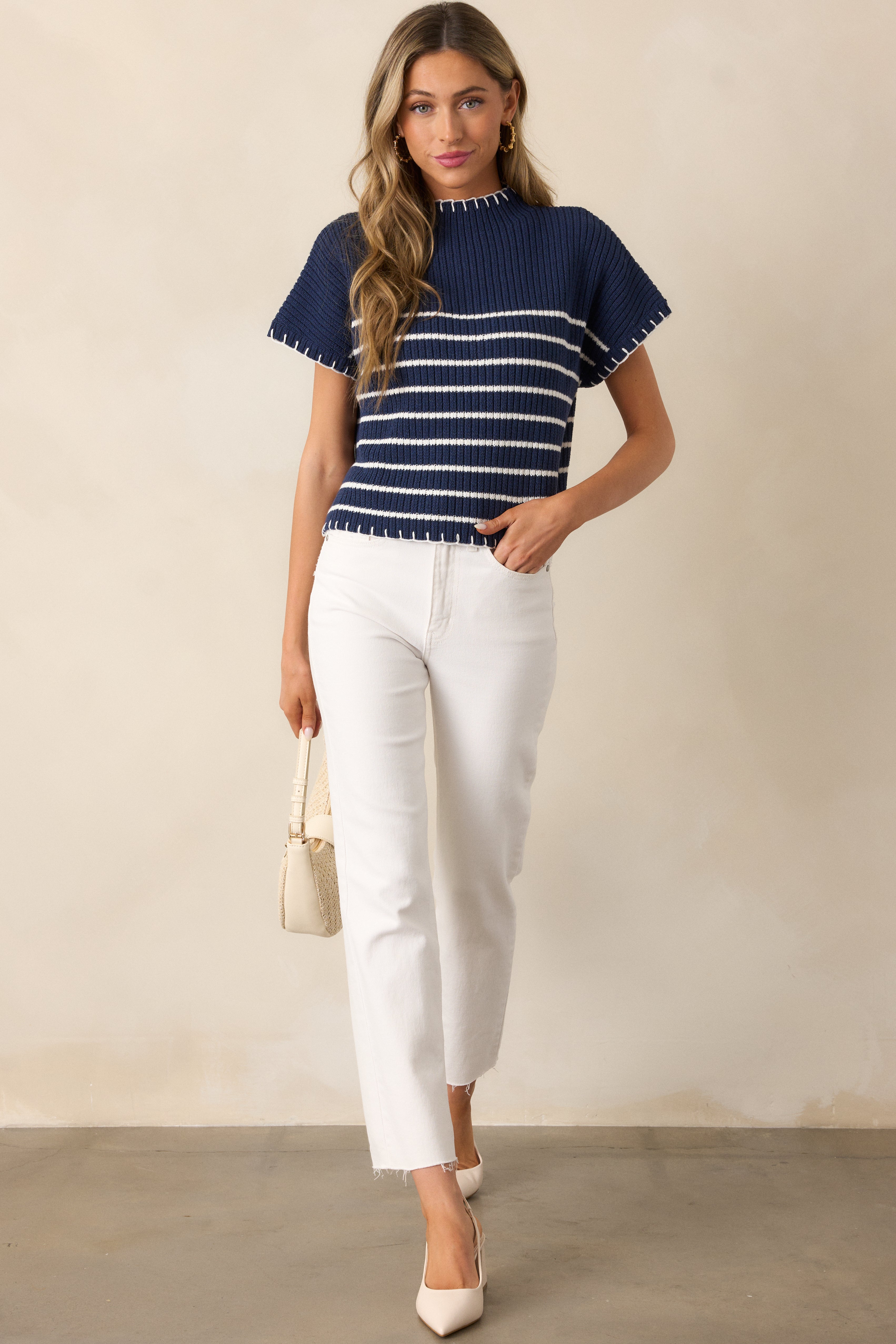 A full-length view of a navy sweater featuring a mock neck, cap sleeves, and white stripe detailing extending from the top of the bust to the hemline.