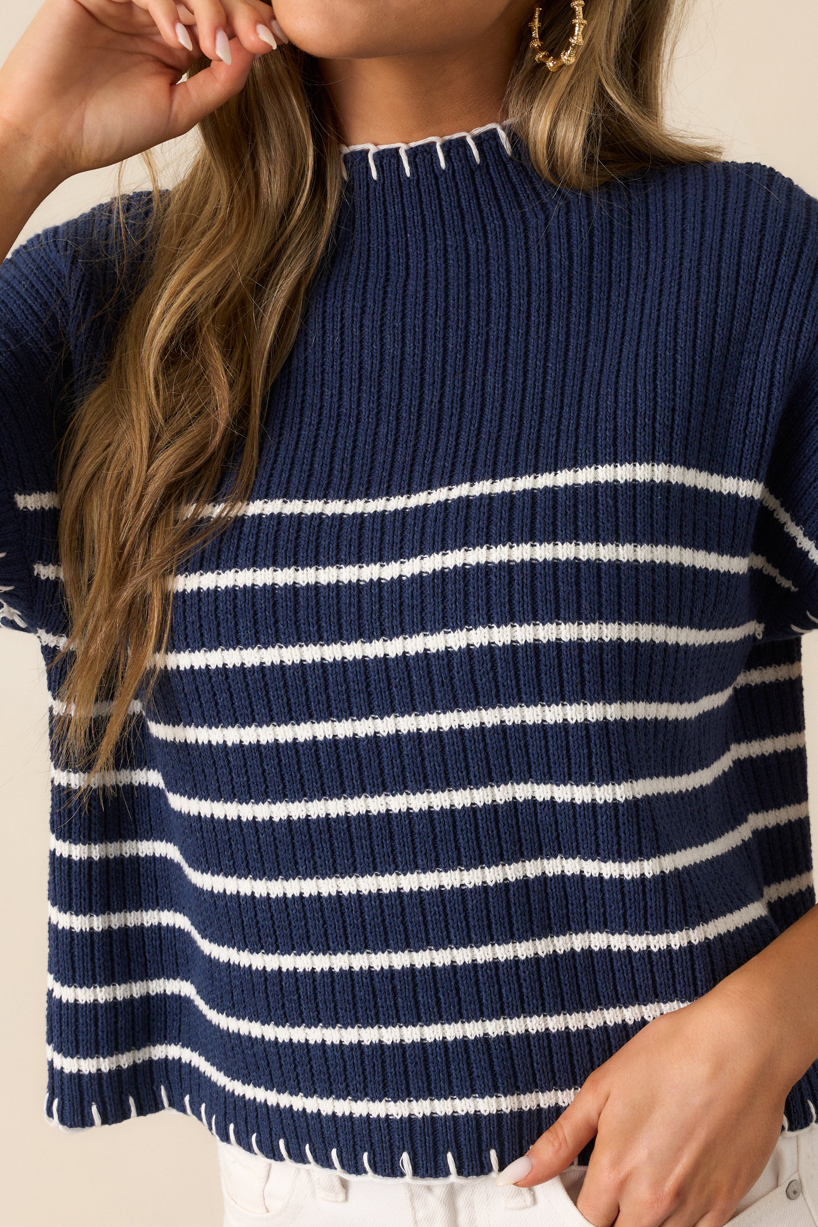 A close-up view of the navy sweater's white whipstitch detailing on the hem, showcasing its intricate craftsmanship.