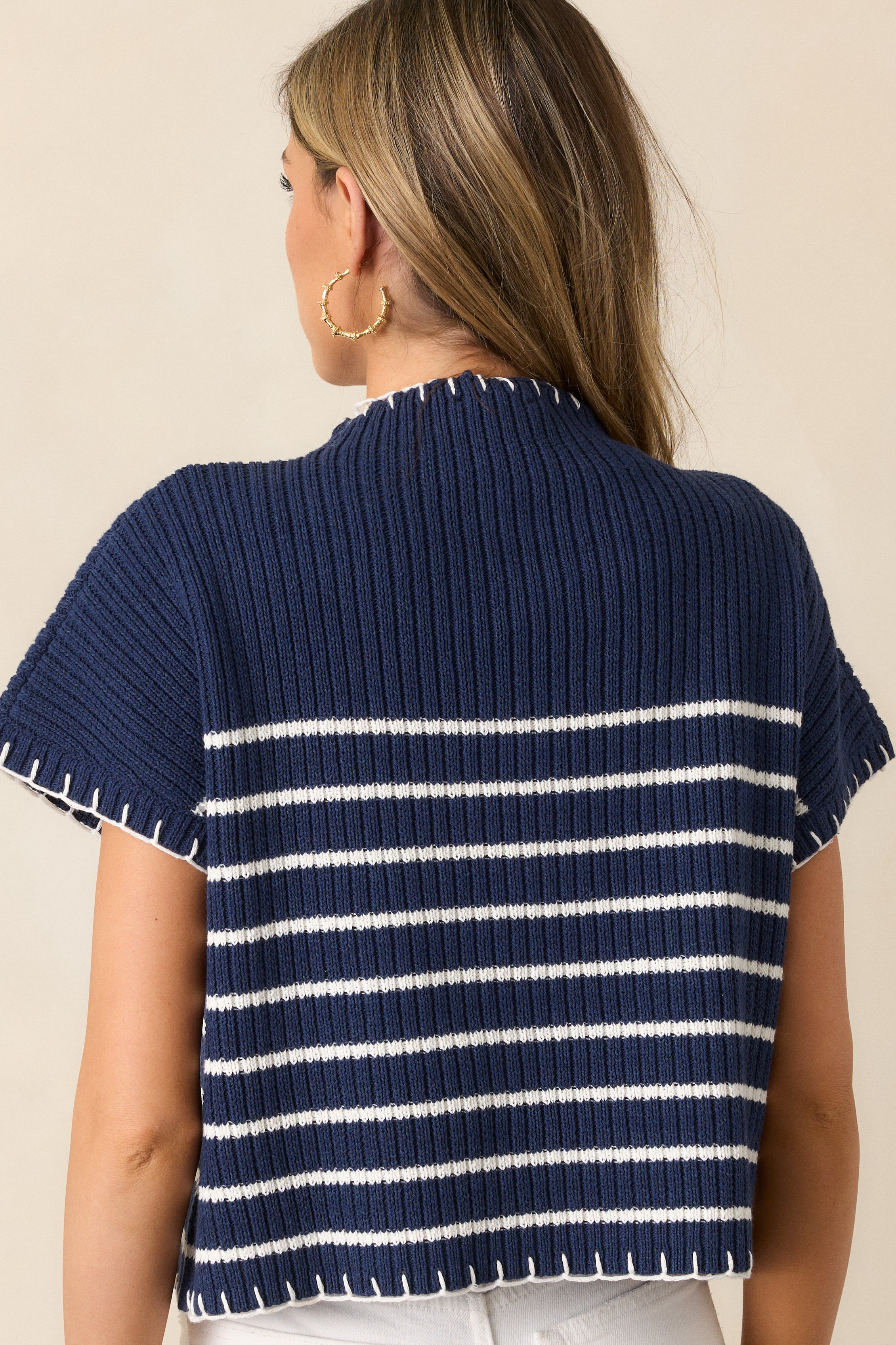 A back view of the navy sweater, highlighting its seamless construction and clean design with white whipstitch accents.