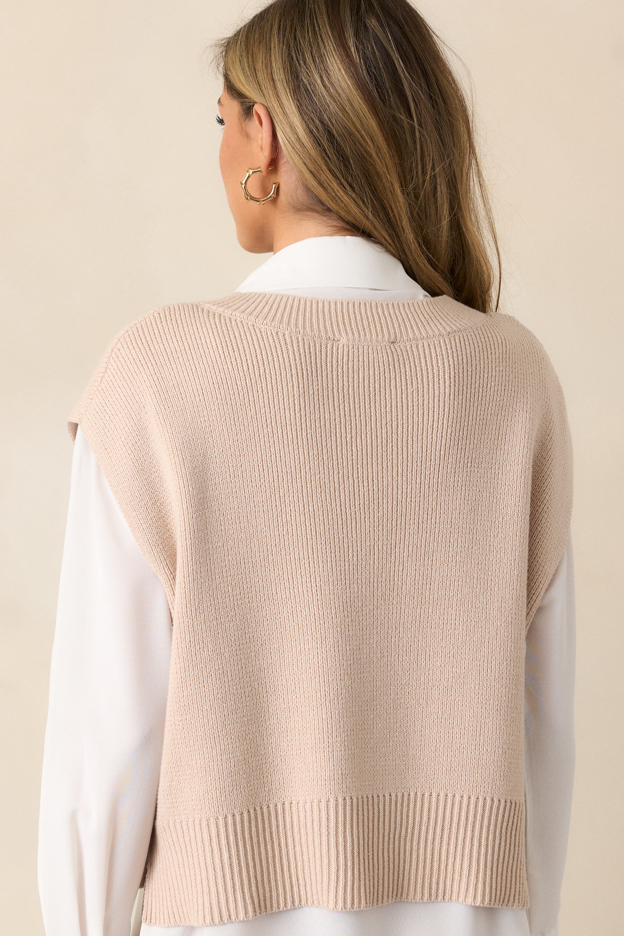 Back view of a beige sweater top highlighting the overall fit, thick hemline, side slits in the hem, and short sleeves.