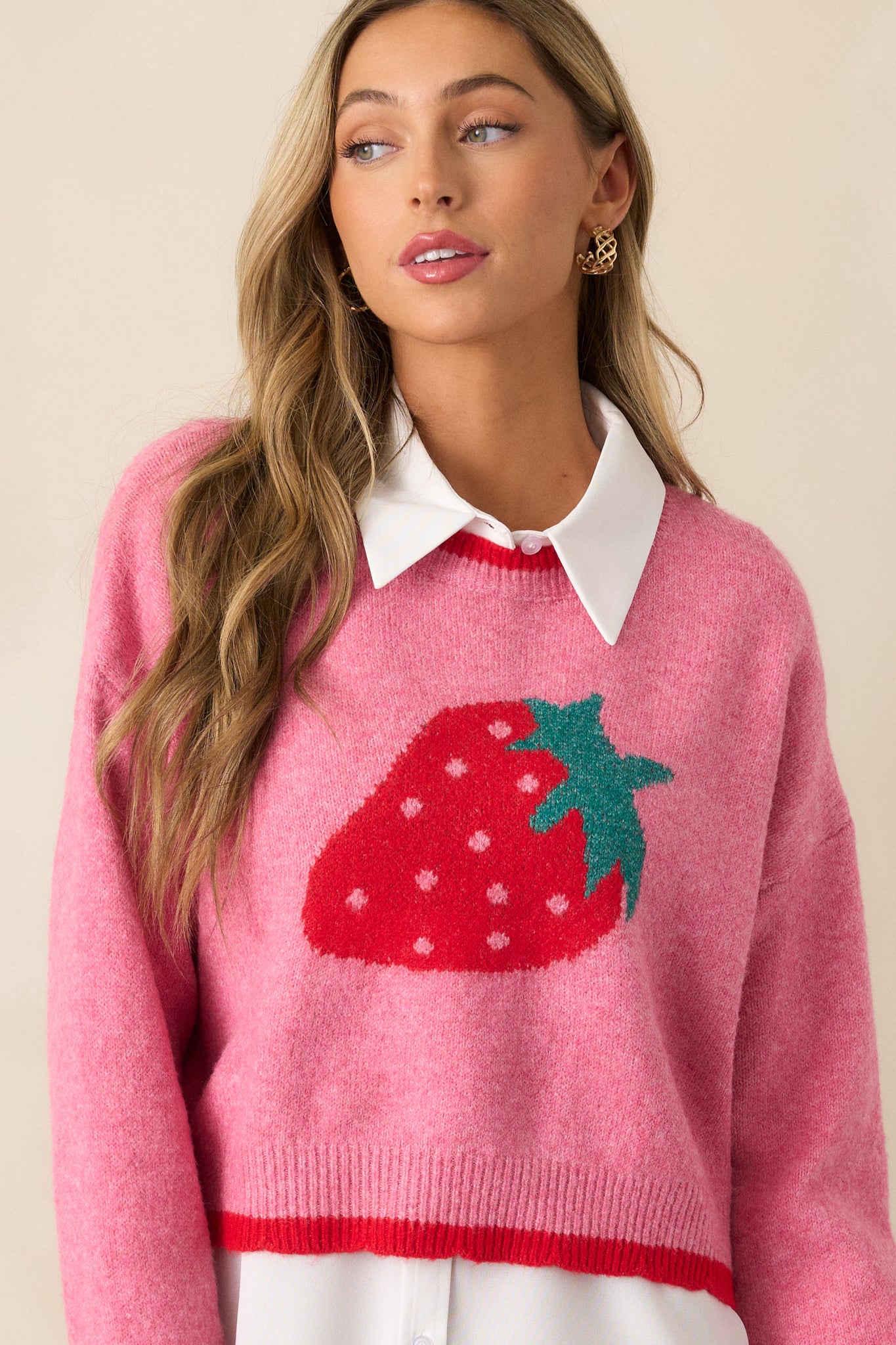 A cheerful close-up of the strawberry design and lively red trim on the neckline of a pink sweater.