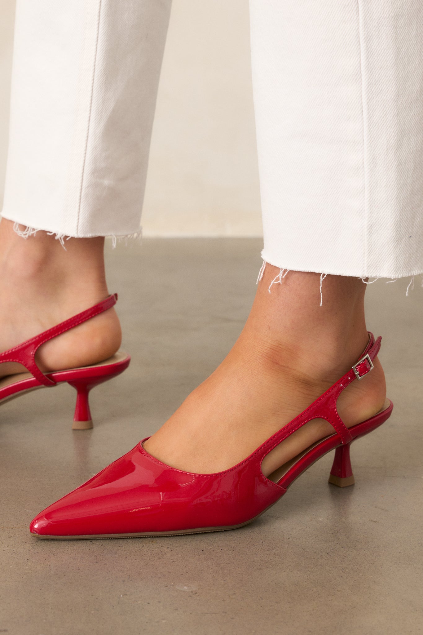 A close-up of the red heels showcasing the small gold buckle detailing, pointed toe, and elegant side cutout detail.