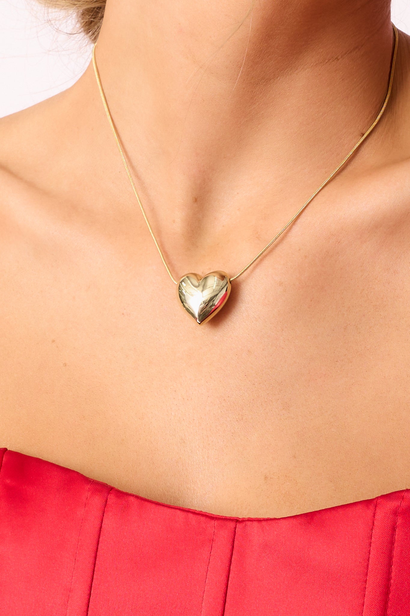 A detailed close-up of the smooth gold heart pendant and the thin chain, focusing on the polished finish and lobster clasp.