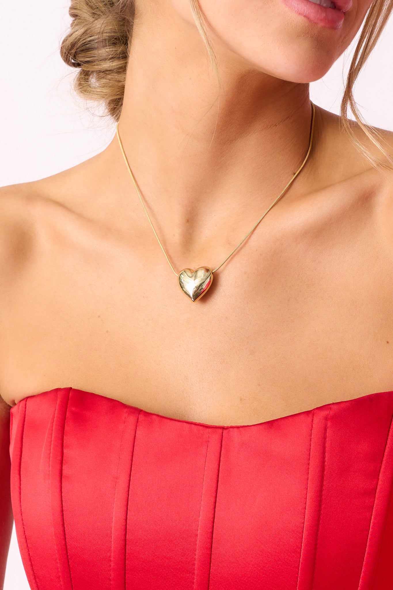 A delicate gold necklace featuring an extremely thin chain and a smooth gold heart pendant, shown from a side angle.