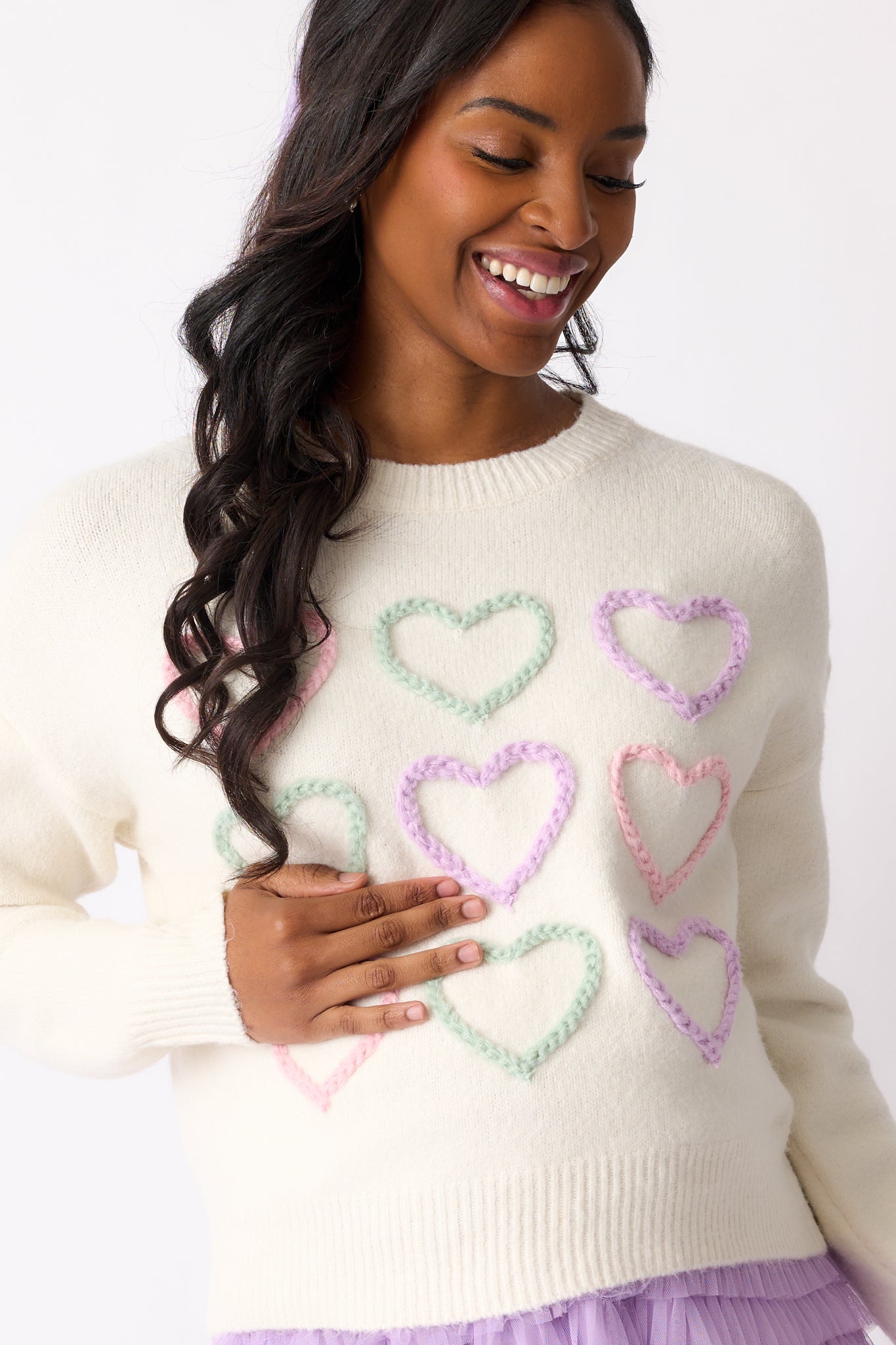 A close-up view of the colorful heart stitch detail on the front of the ivory sweater, showcasing the intricate and cheerful design.