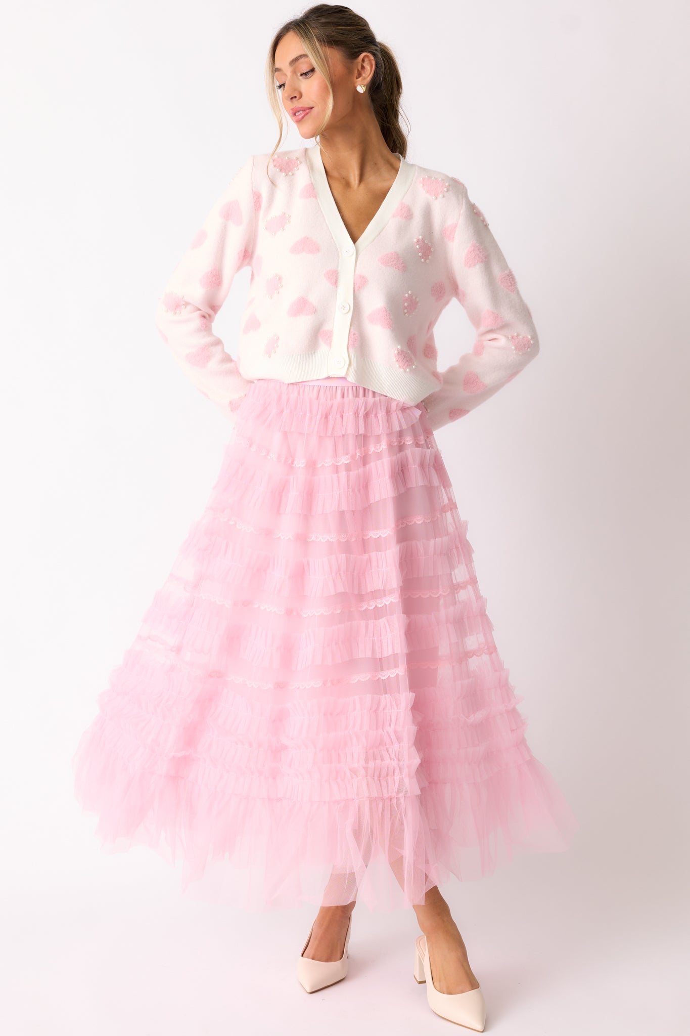 A full view of the light pink skirt featuring an elastic waistband, a ruffle tulle overlay, and beautiful lace detailing, falling to midi length.