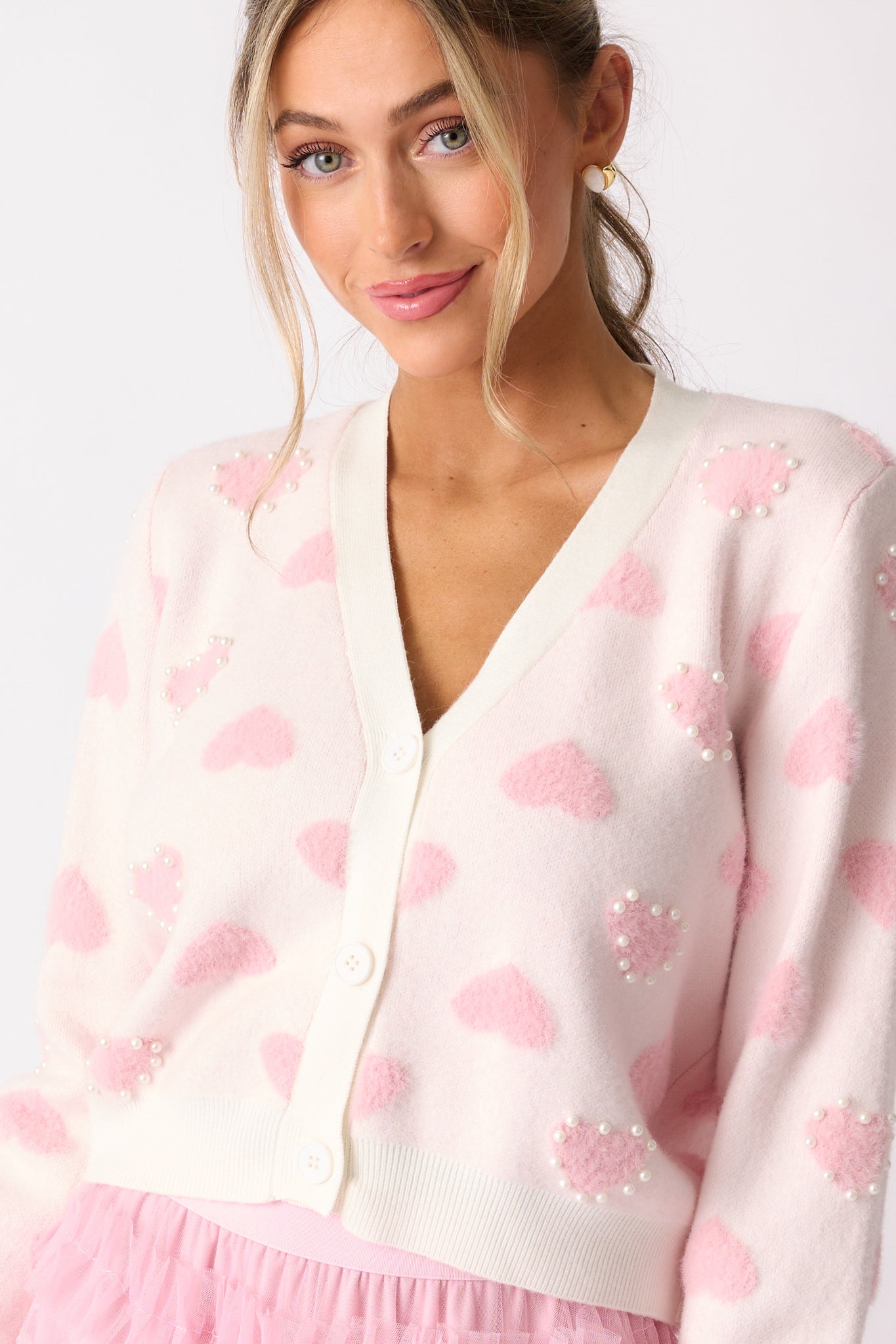 A close-up of the cardigan’s button-front detail with pink fuzzy hearts, long sleeves, and ivory pearl accents.