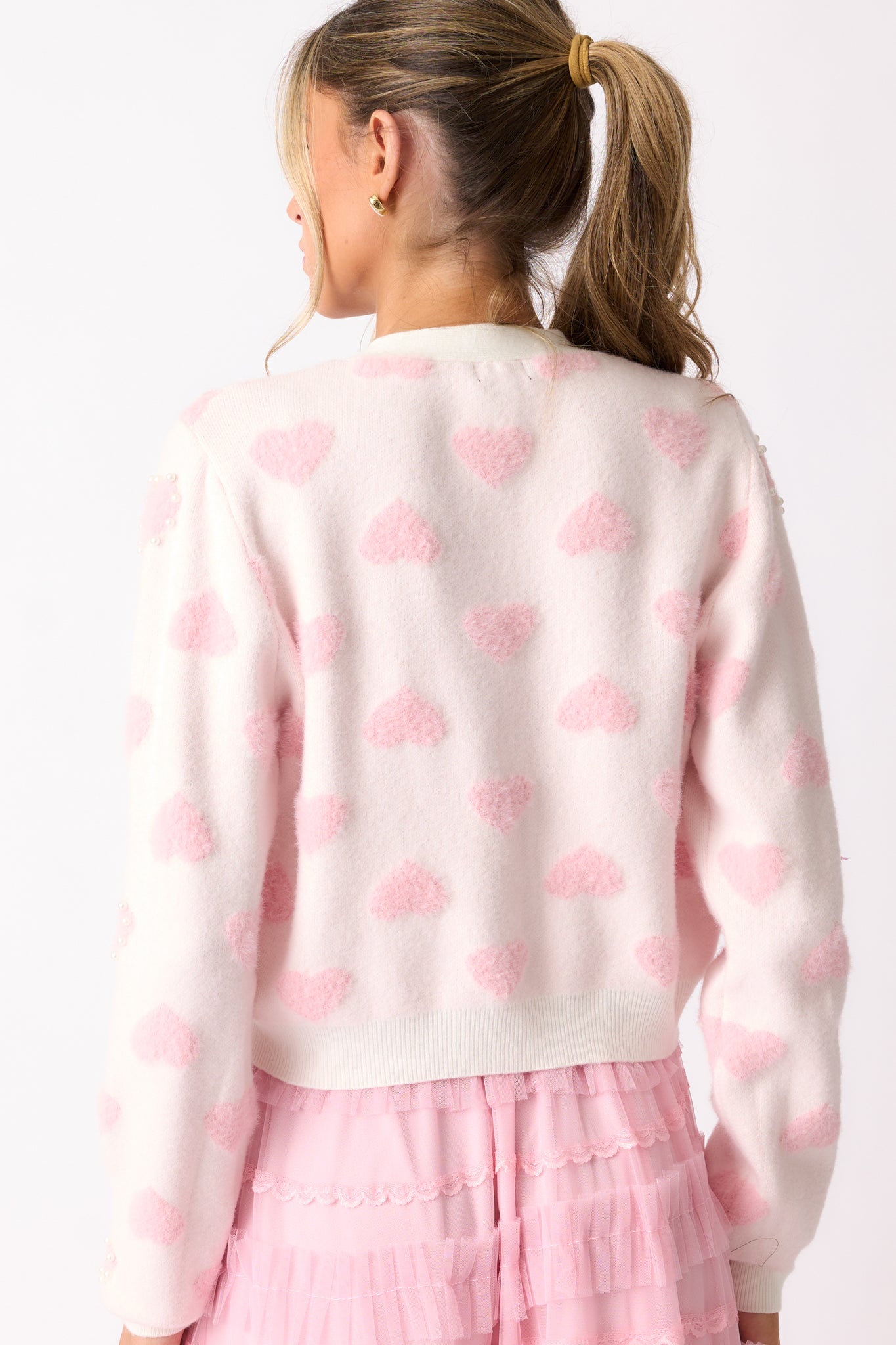 The back of the pink cardigan showing its seamless design, long sleeves, and consistent heart print pattern.