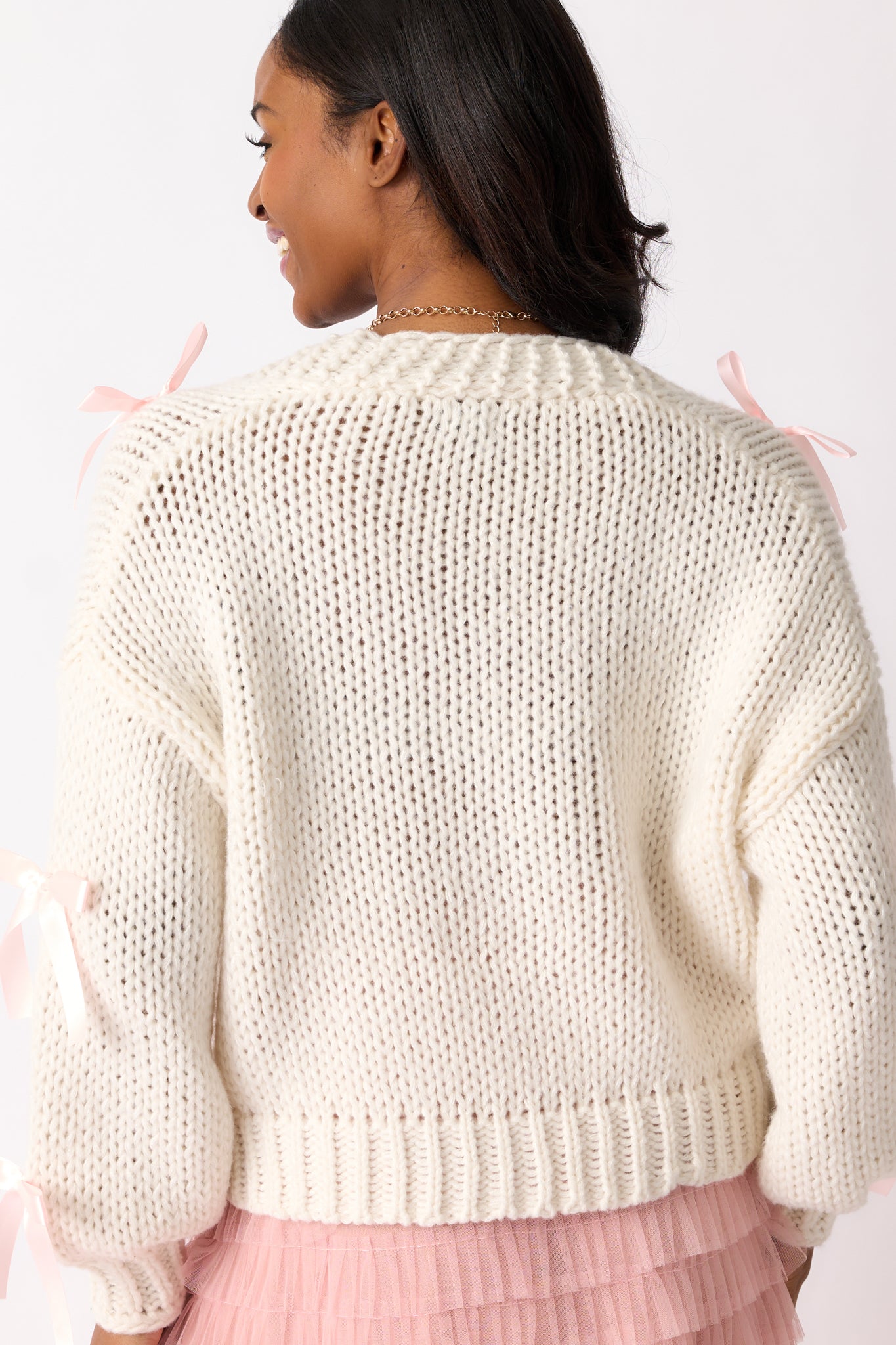 A back view of the cardigan, showing the clean, simple ivory knit design with the long sleeves extending seamlessly from the shoulder.