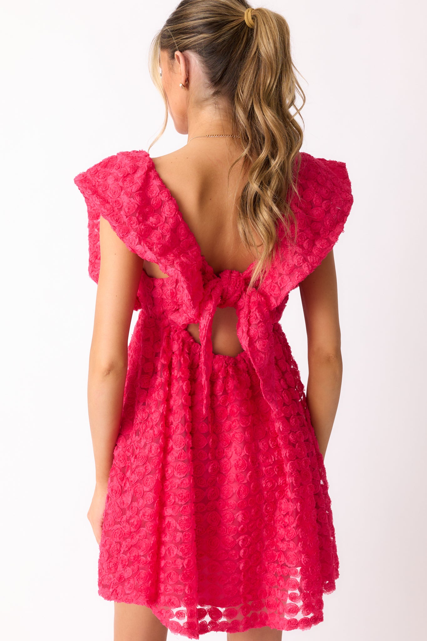 A back view of the hot pink mini dress, featuring the self-tie back detail and the smooth flow of the embroidered fabric.