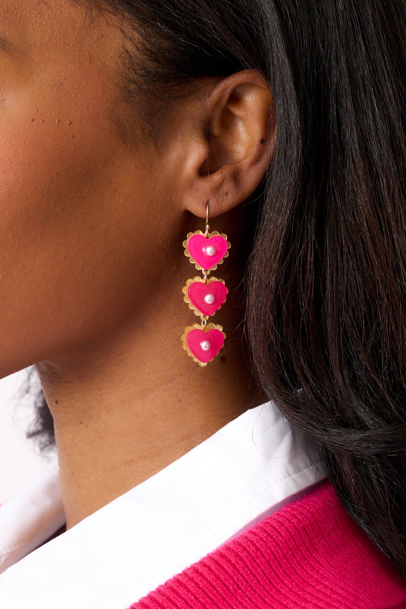 A zoomed-in view of the earring, highlighting the sparkling pink glitter hearts, the delicate ivory faux pearls in the center, and the secure post backings in fine detail.