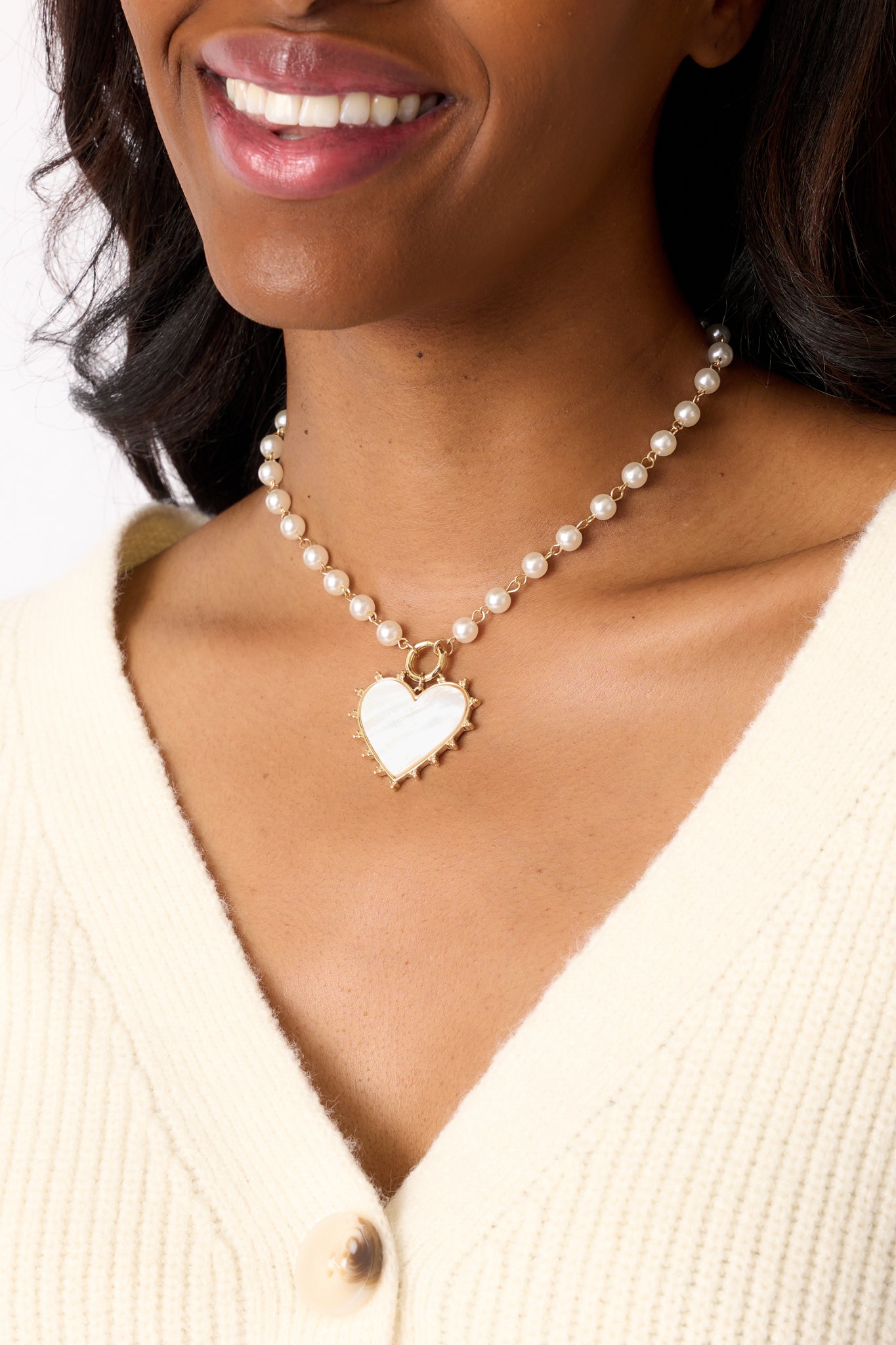 A close angle focusing on the large ivory heart pendant, highlighting its gold spike border and the detailed craftsmanship of the gold jump ring attachment.