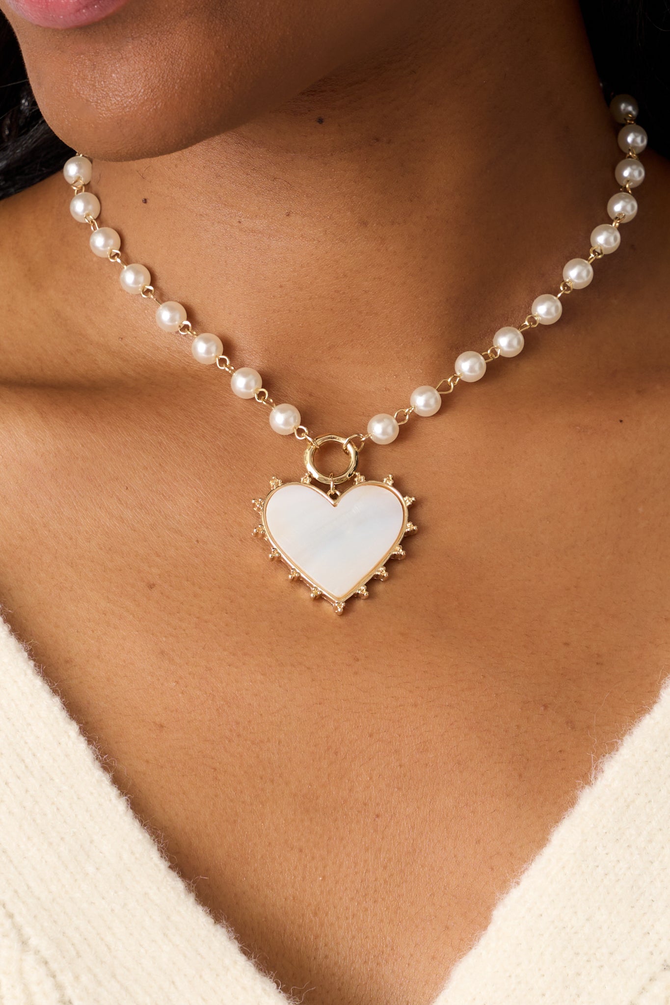 A zoomed-in view of the necklace, emphasizing the glossy pearlescent heart pendant, the intricate gold spikes, the delicate gold and pearl chain, and the lobster claw closure.