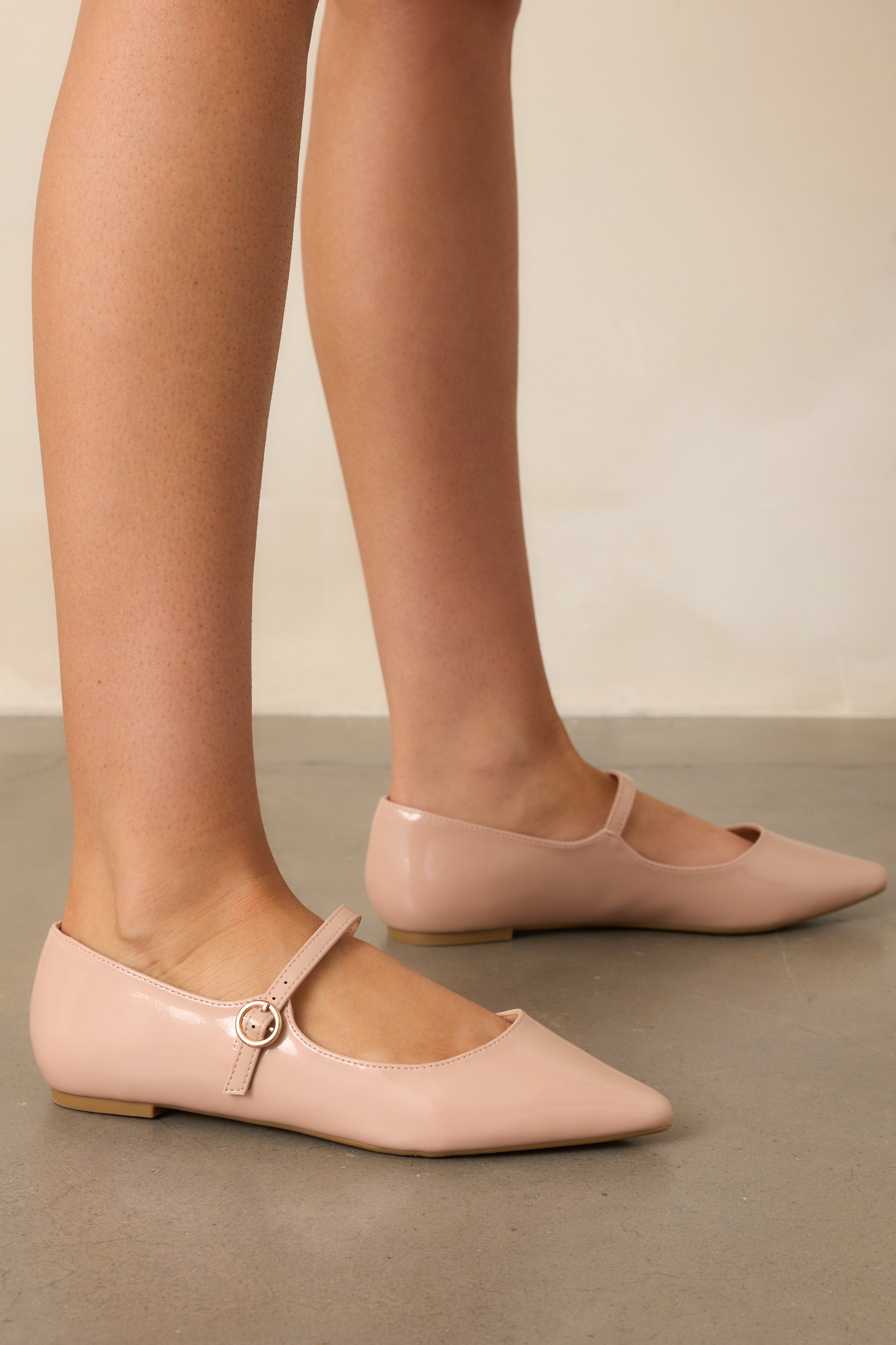 Beige flats with a pointed toe, featuring a sleek material and a decorative buckle across the foot strap.